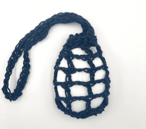 A blue soap saver in the style of a wide open stitch bag with a large loop for hanging and drawing closed at the top. The holes in the bag are about 2cm wide and inside there is a white bar of soap.