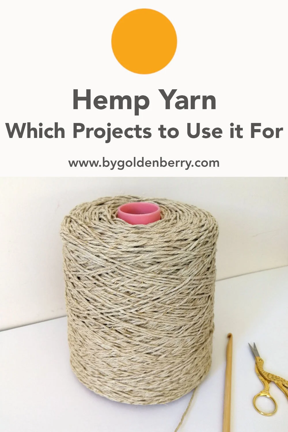 A large cone of oat coloured hemp yarn is sat on a white surface. The wall behind is magnolia. The cone in the centre is baby pink and the strands of the yarn have clear definition. There is a wooden hook and a silver and gold pair of stork scissors.