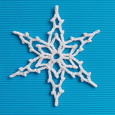 A birds eye view of a white Lacey crocheted snowflake with a central flower shape and six points. The background is stripy blue.