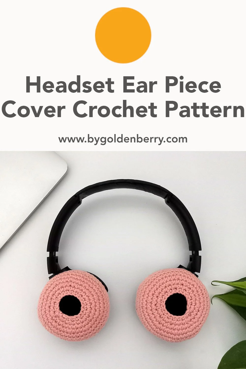 A birds eye view of the pastel pink ear piece covers on a set of black headphones. The headset is sat on a white surface. The covers have an open centre showing a pitch black hole in the middle. In the top left is the corner of a silver laptop.