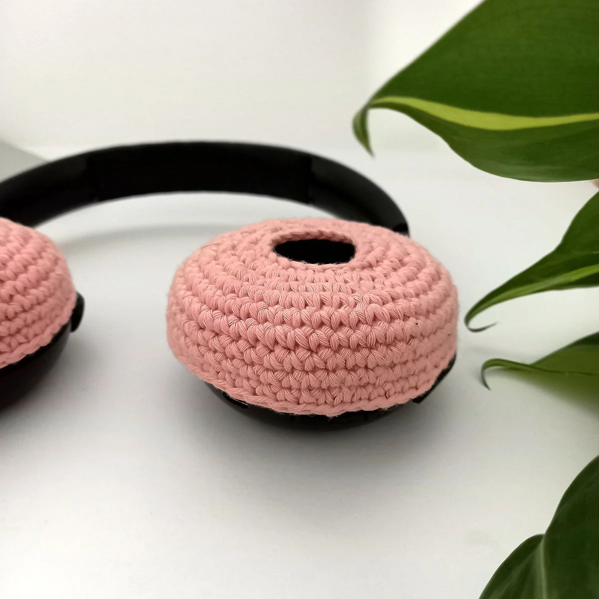 A side view of the right side headset ear piece with the pastel pink cushion cover. The left ear piece is creeping into shot on the left. There is green foliage on the right of the photo. The edges of the cover are about an inch deep.