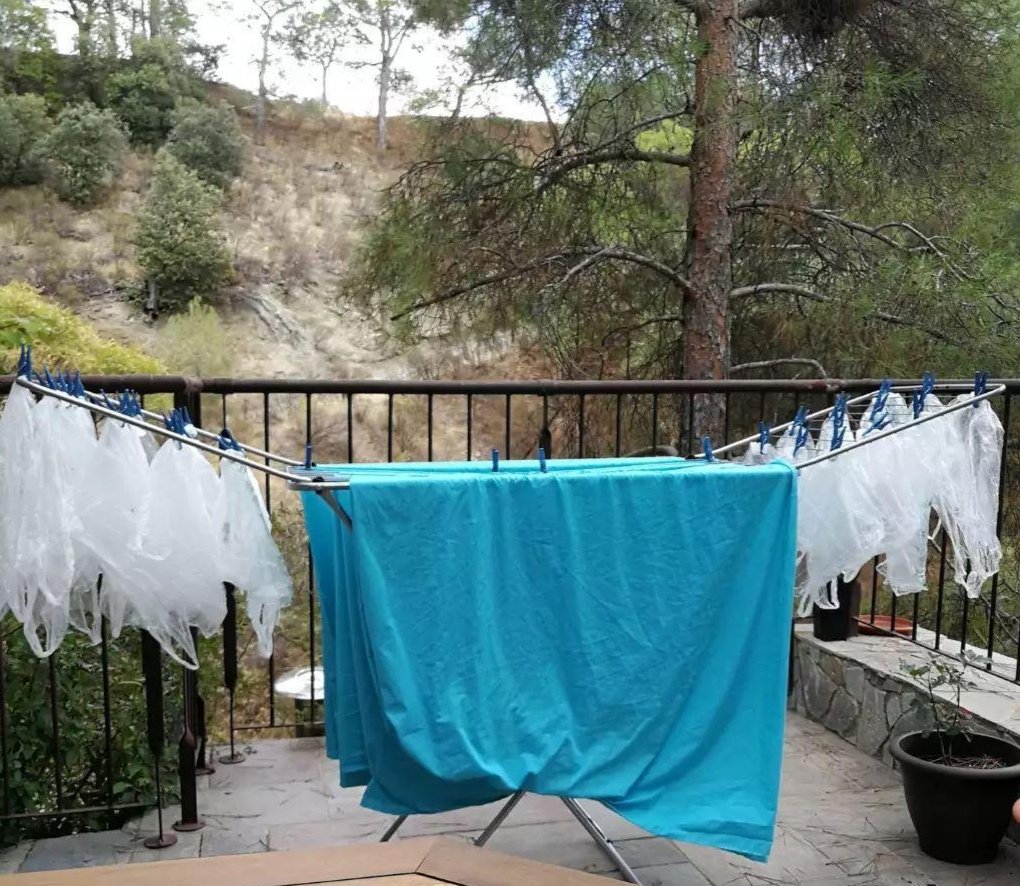 A clothes horse is outside on the veranda with sky blue bed sheets on plus about 50 plastic bags. The background is wooded and hilly.