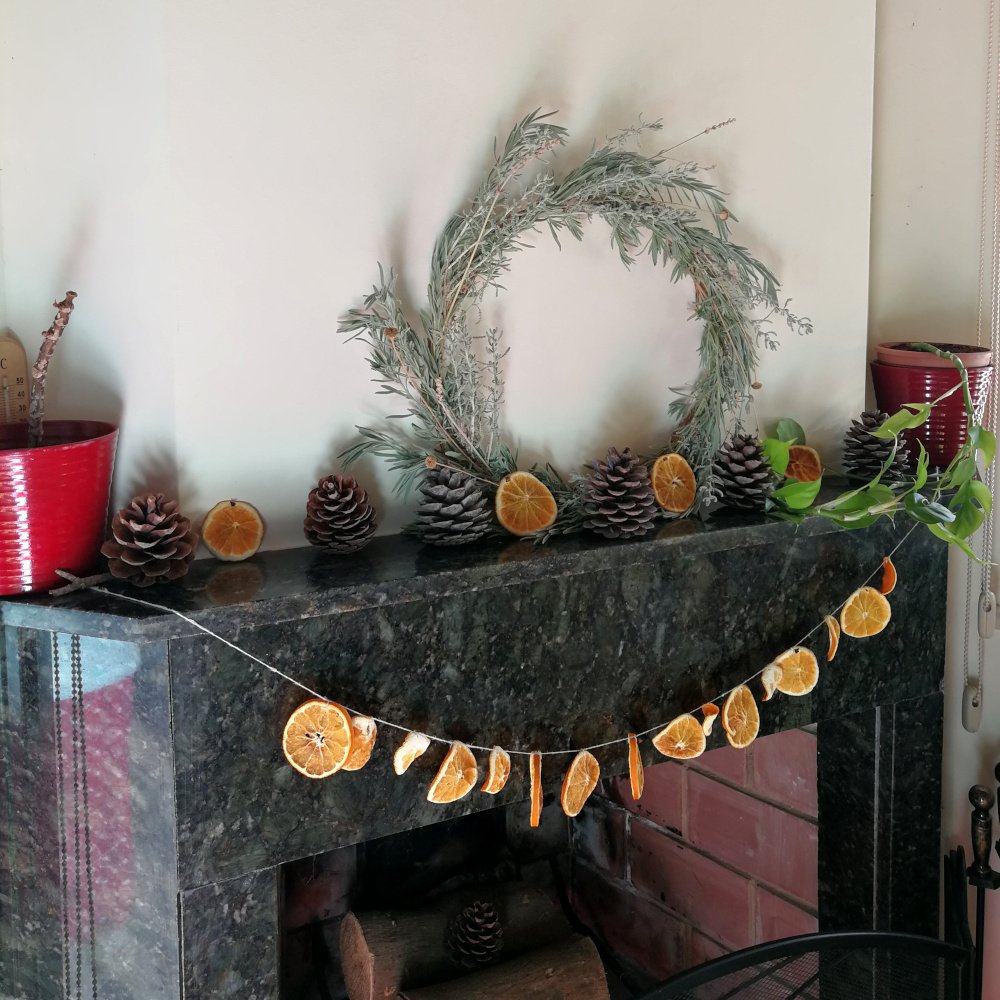 There is a dark grey marble mantlepiece with an off white chimney breast. It has the circular wreath sat in the centre with pine cones and orange slices to the left and right. There is an orange slice garland hanging from the each corner.