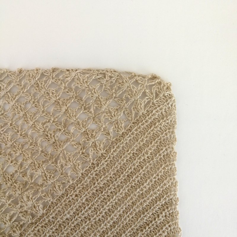 A square piece of the dress is laid on an off white background.  The dress is coming in from the left hand side and shows the top shell section and the hdc bias section with diagonal the join from bottom left to top right.