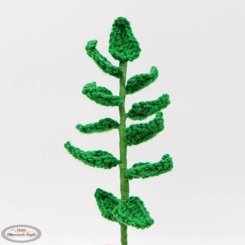 A single long, green stem is stood centrally in the frame with 11 small leaves divided between the left and right with one at the very top. The background is off white.