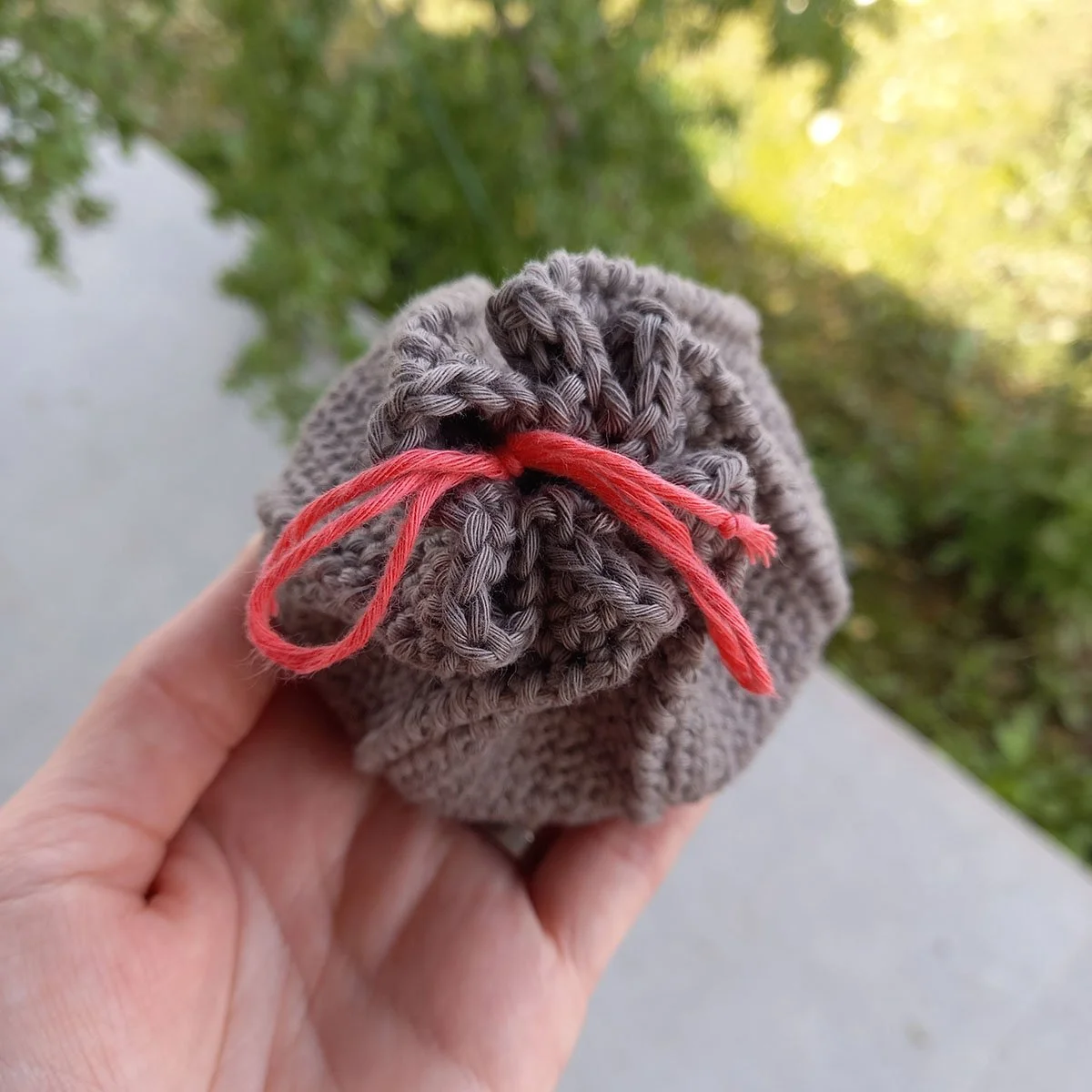 A birds eye view of the top of the coin purse. The top is drawn together with a bright pink drawstring tied into a bow. The pouch is gathered together in 6 sections which creates a kind of 6 pointed shape at the top. The background is green and grey.