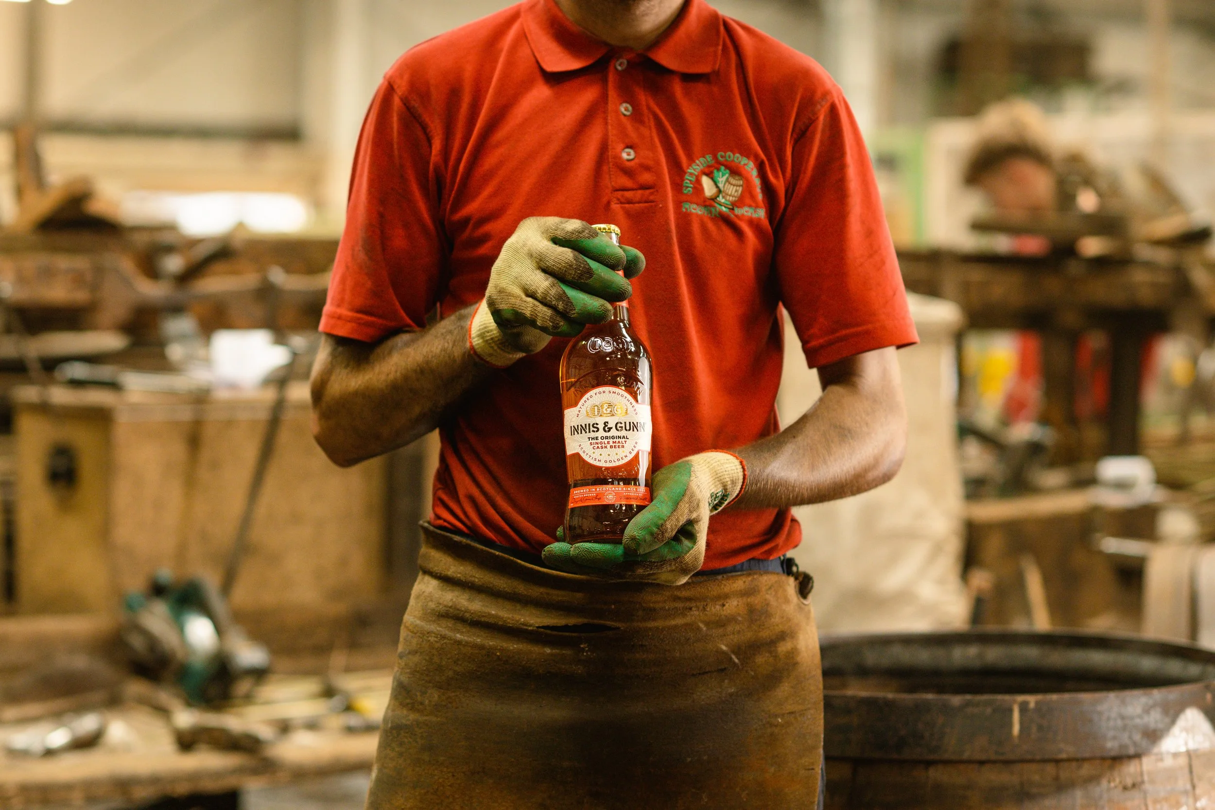 Person holding a bottle of Innis & Gunn whiskey in a workshop or factory setting.