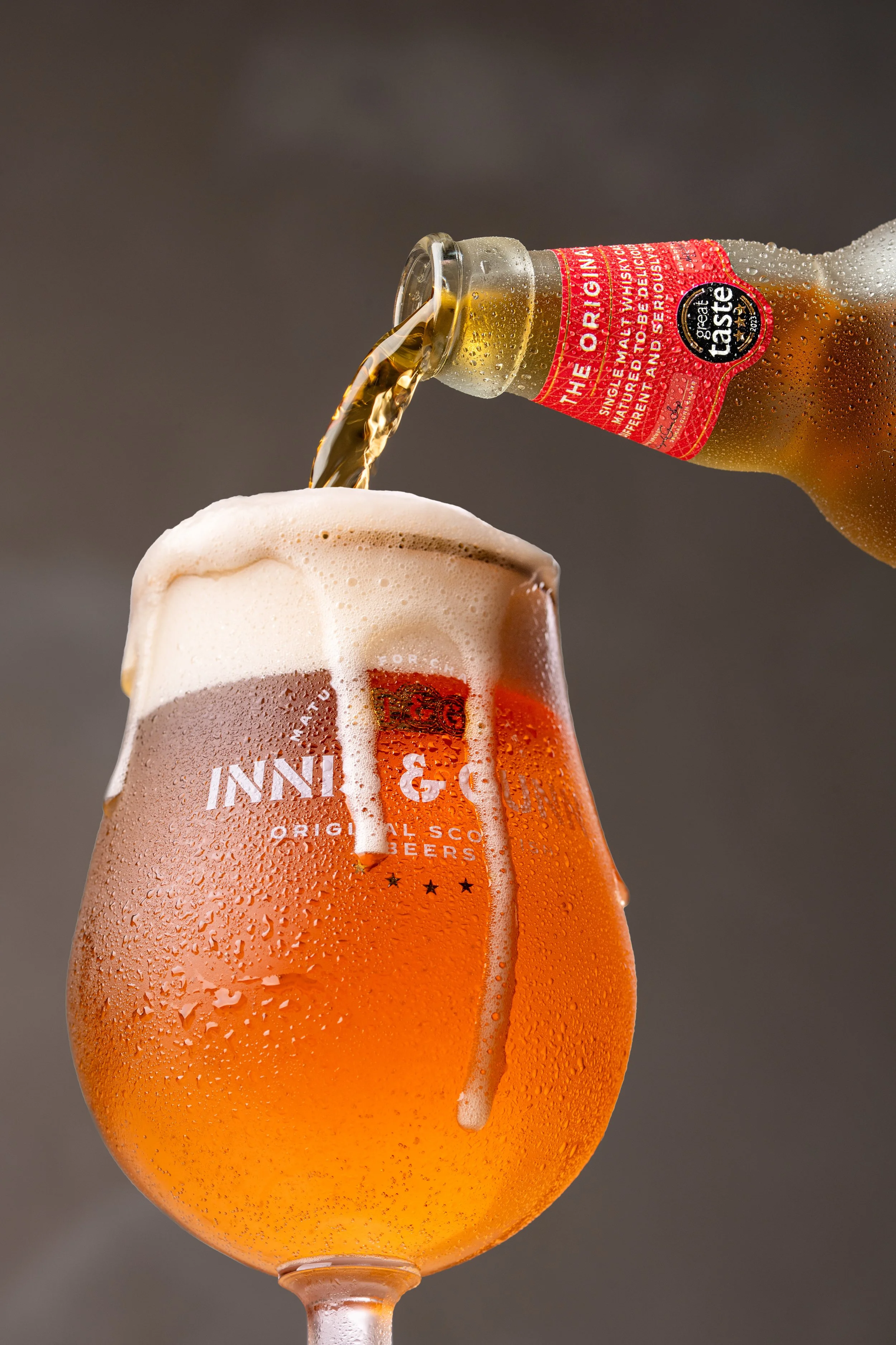 Pouring beer from a bottle into a branded beer glass with foam on top and condensation on the glass.