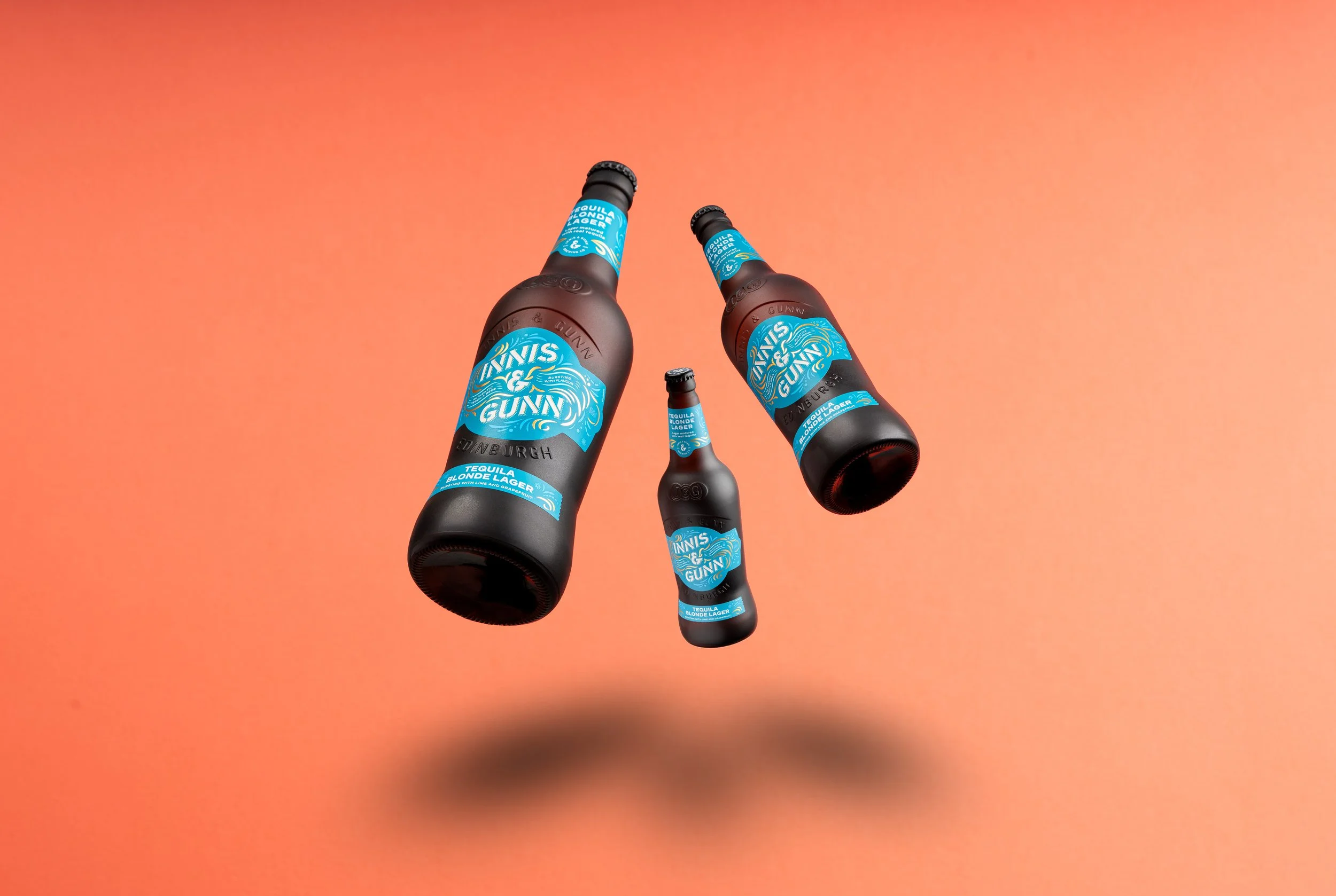 Three bottles of Gunn & Sun tequila blonde lager floating against an orange background.