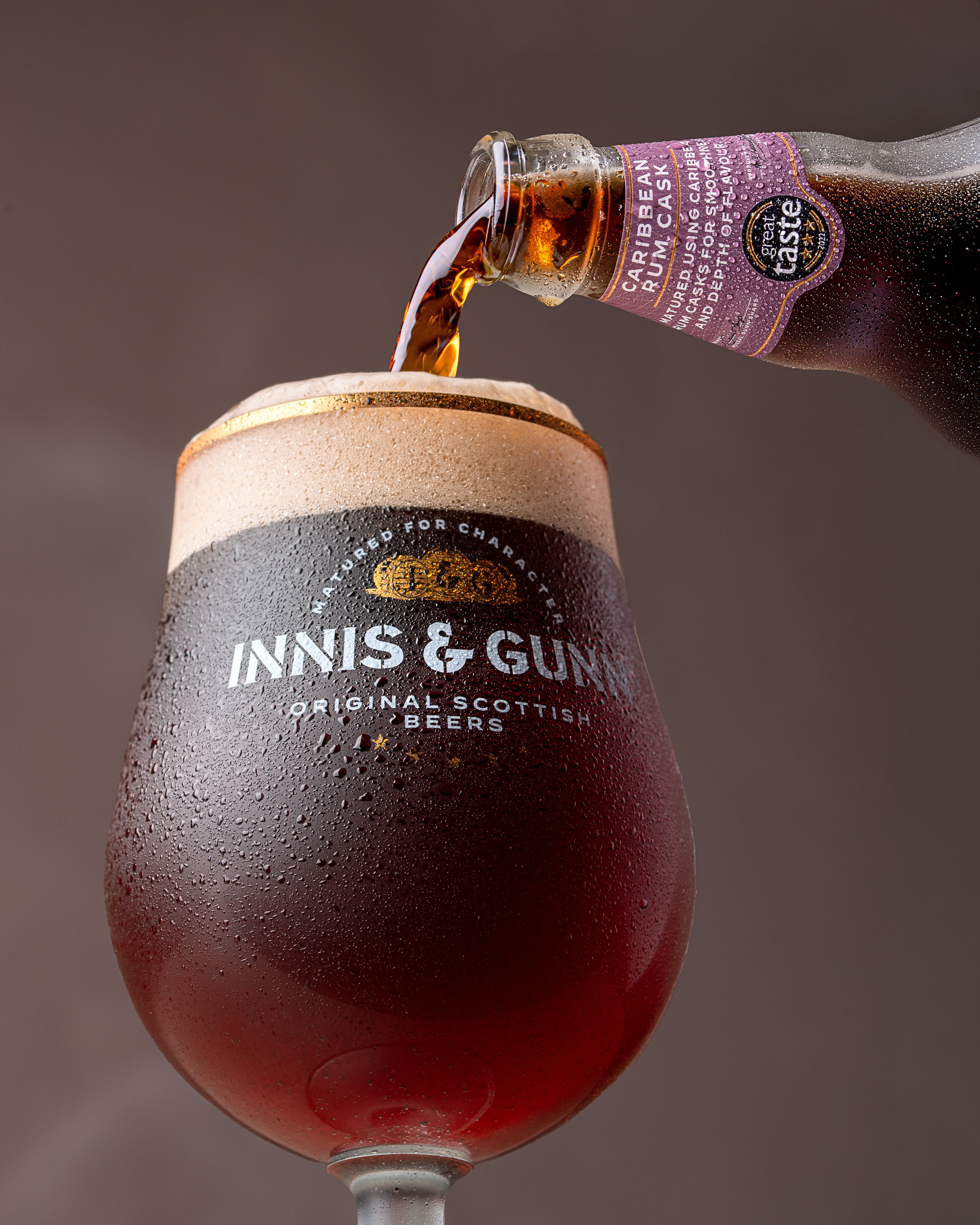 A glass of dark beer with condensation being poured from a bottle labeled Caribbean Rum Cask, with the brand name Inniskillin on the glass.