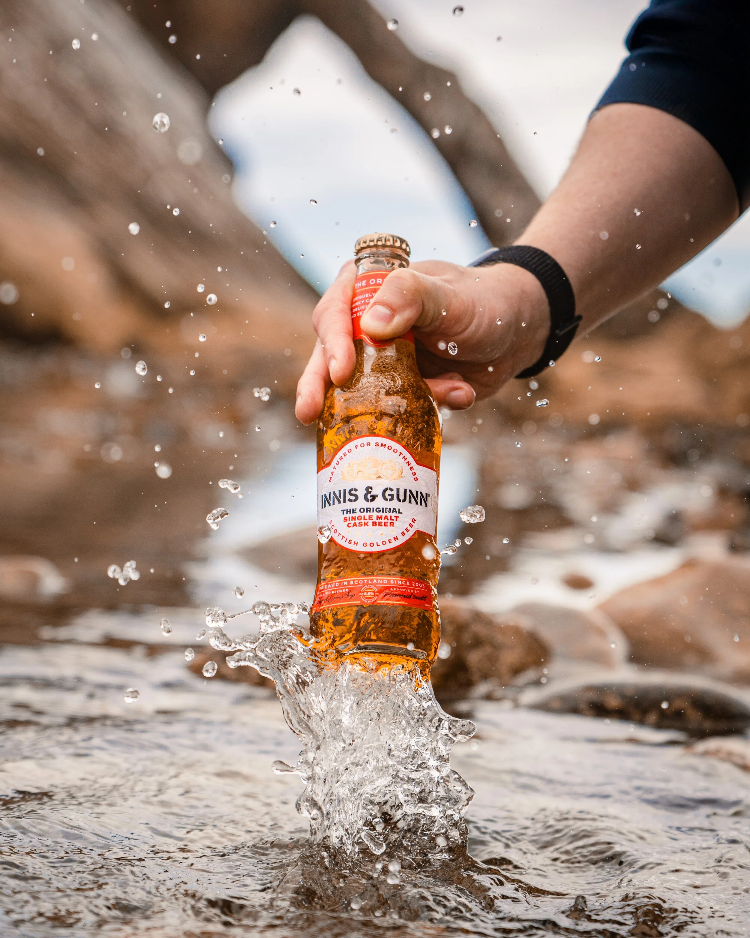 Person holding a bottle of Innis & Gunn beer in water at a river or stream