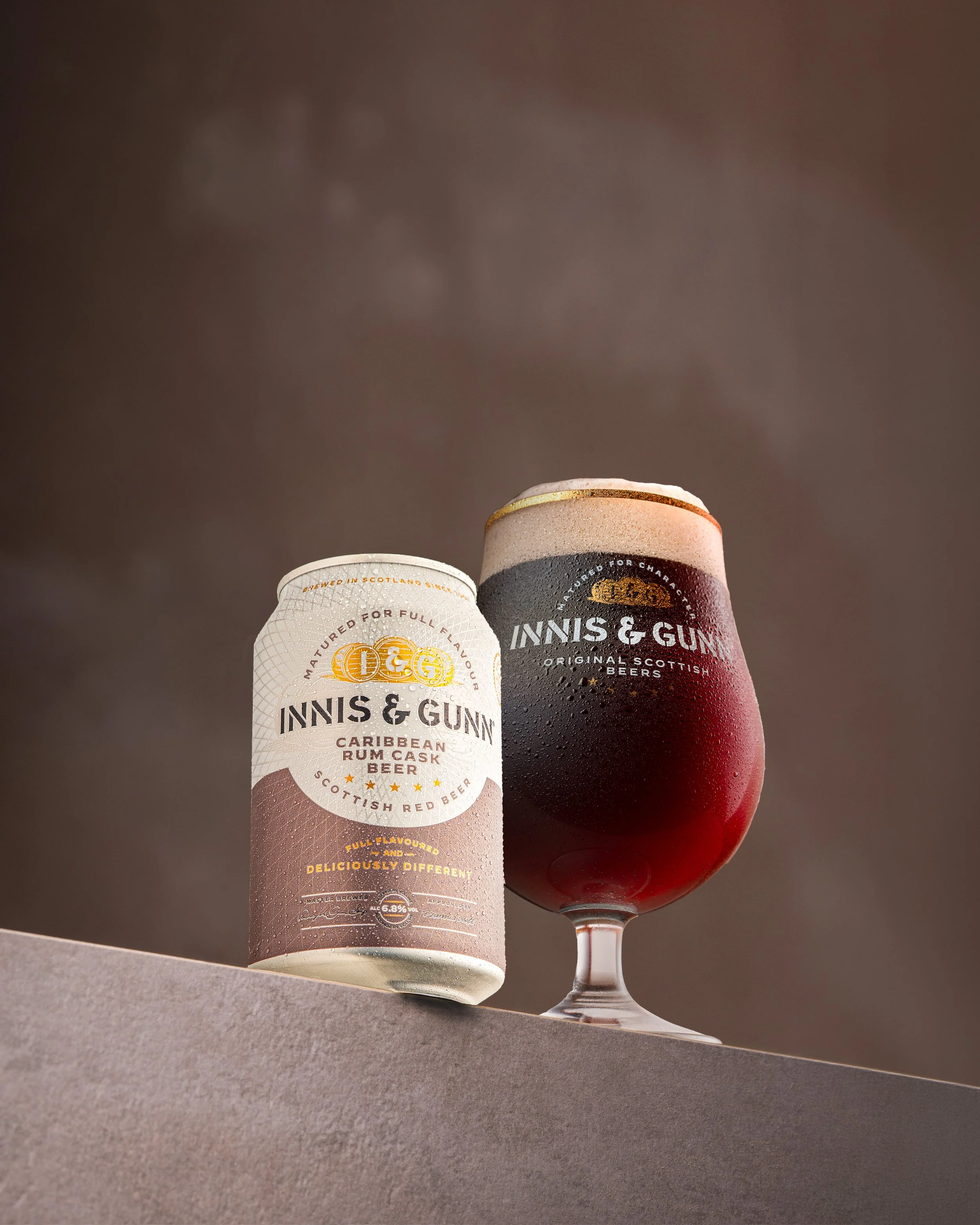 A can of Inniskillin Caribbean Rum Cask Beer and a glass of dark beer, both with the Inniskillin logo, set on a flat surface against a plain background.
