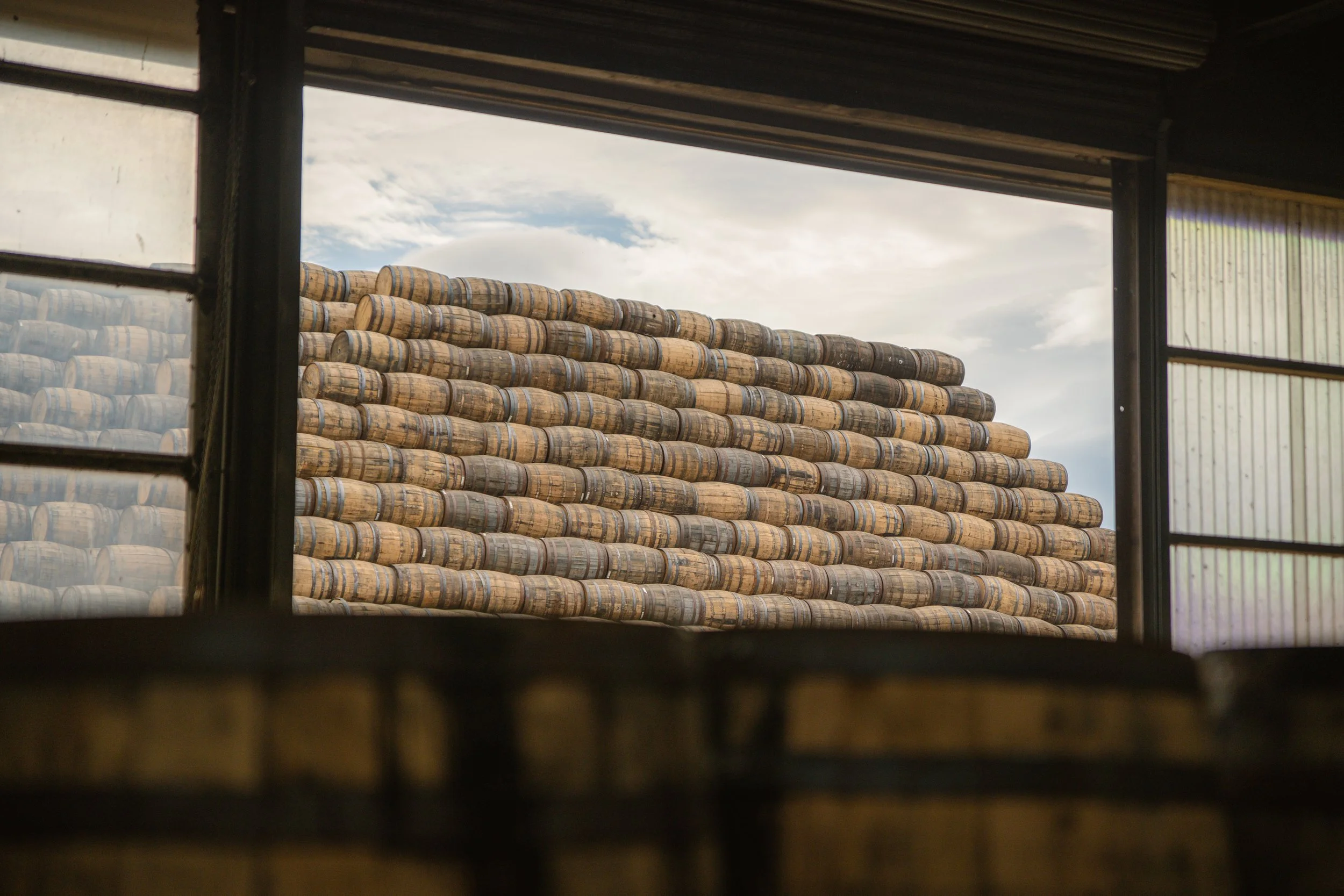 Stacked barrels viewed from inside a building through a window.