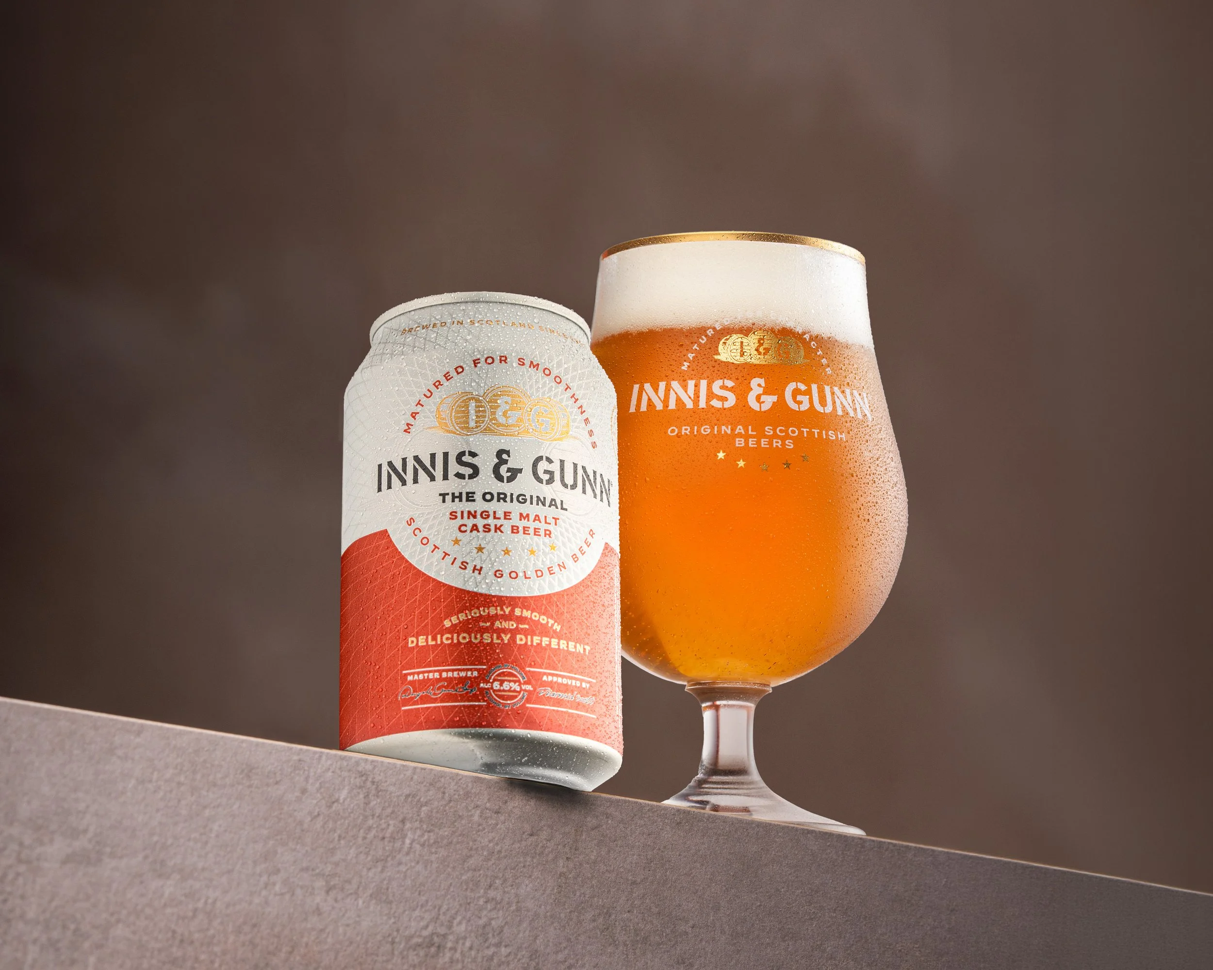 A can of Innis & Gunn single malt cask beer and a filled beer glass positioned on a ledge against a gradient background.