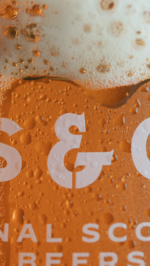 Close-up of a beer bottle with condensation, showing white text and bubbles on the orange label.