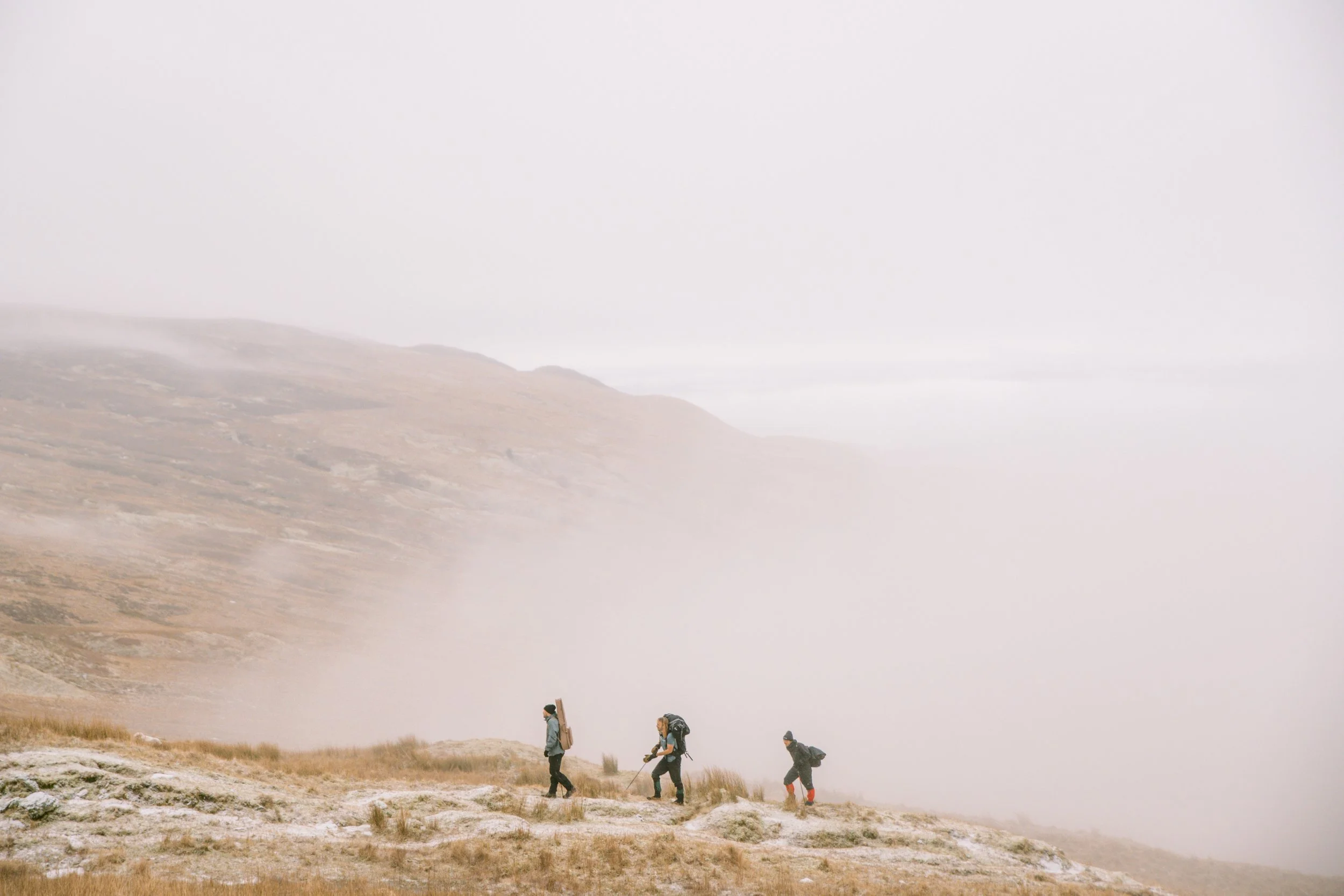 Three hikers walking on a mountain trail surrounded by fog and mist.