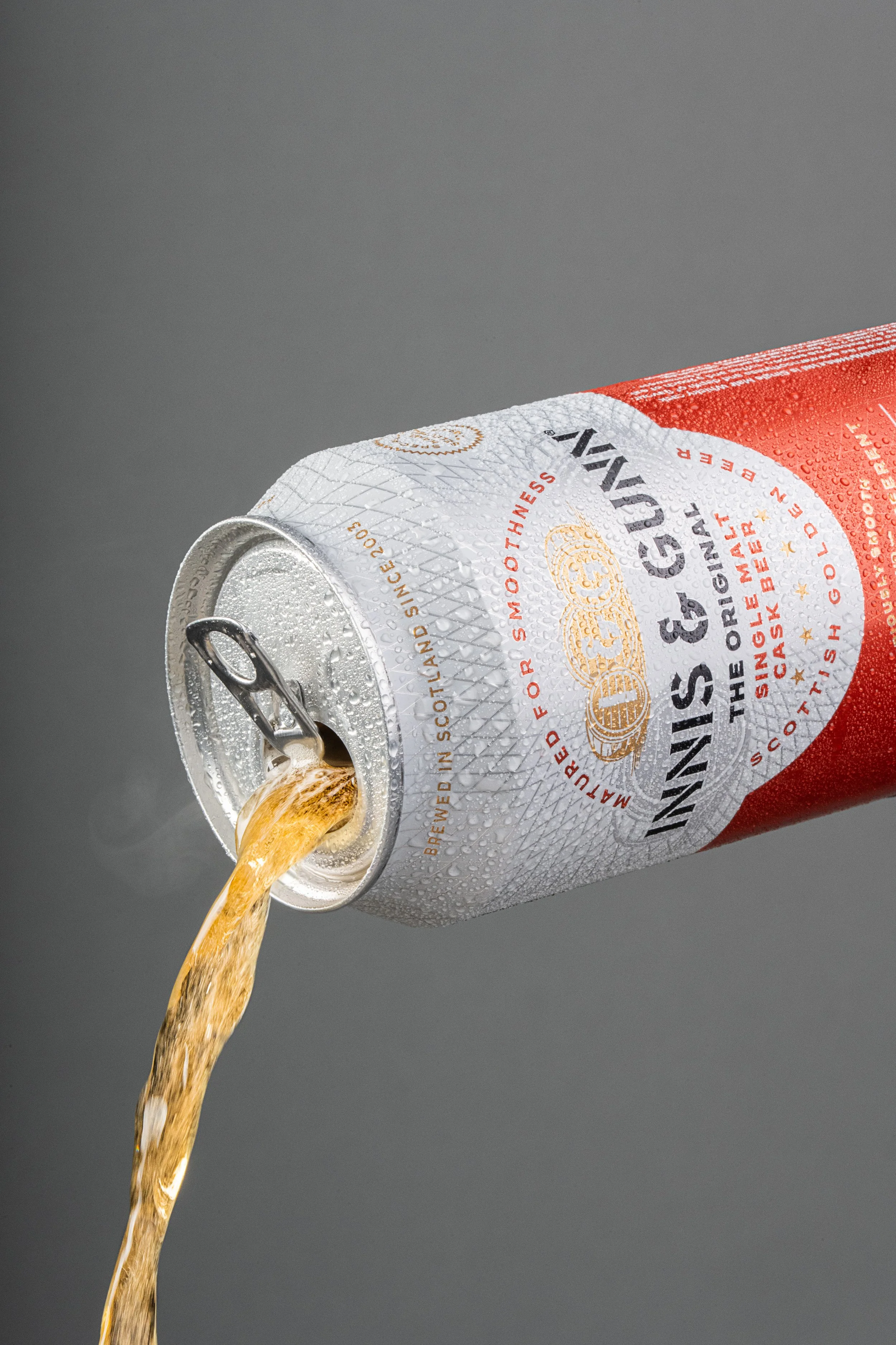 A can of Innis & Gunn beer with beer pouring out of the opened top against a gray background.