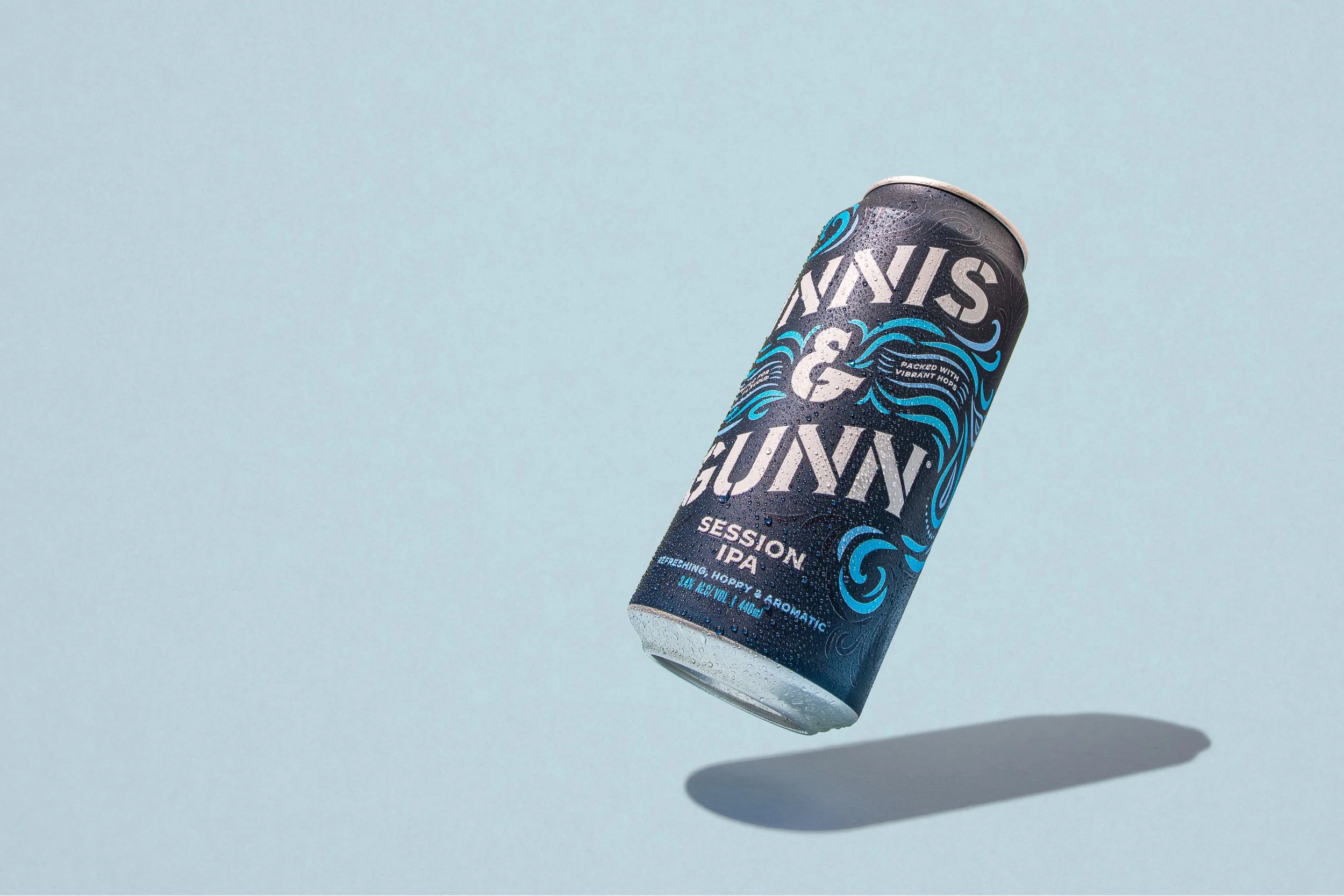 A can of Hop Liquor Hazy & Juicy Session IPA beer with water droplets on the surface and a shadow on a light blue background.