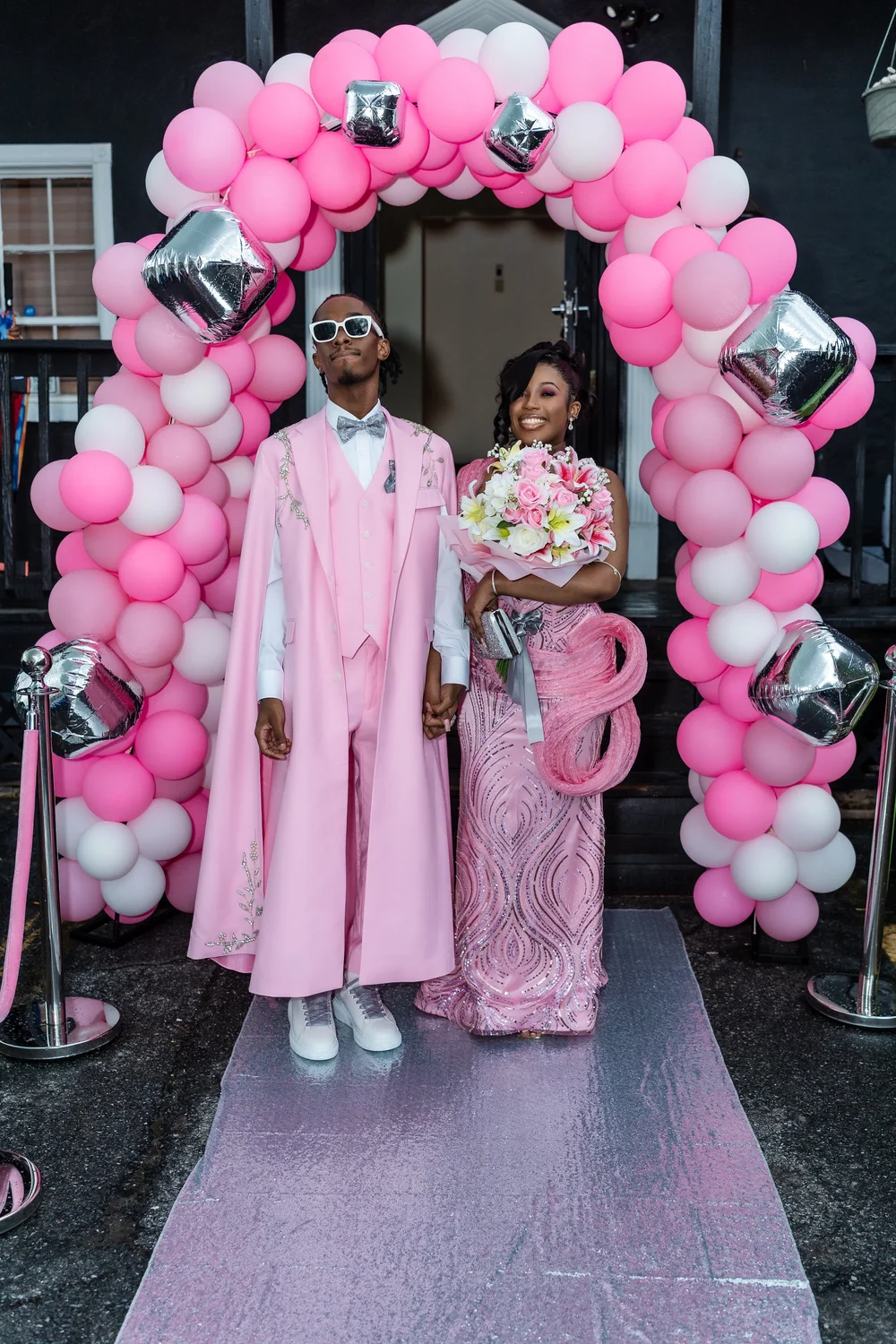 Prom sendoff group in pink beneath a balloon arch