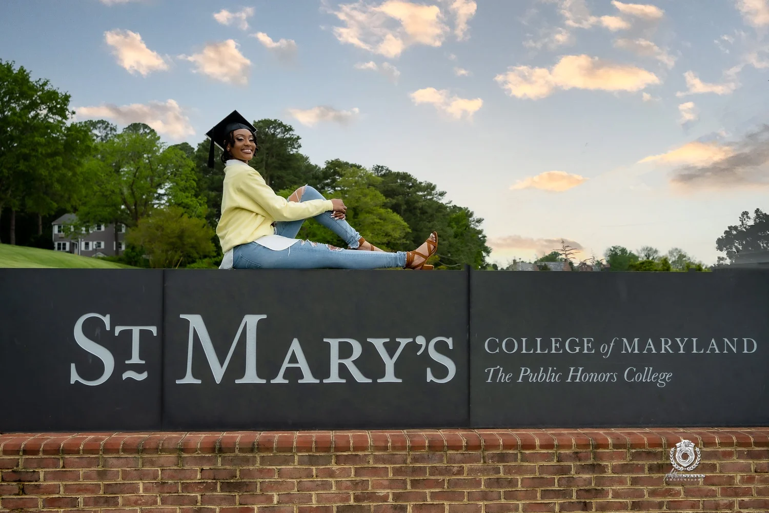 Graduate laughing on the St. Mary's College sign under a bright sky during a senior portrait session