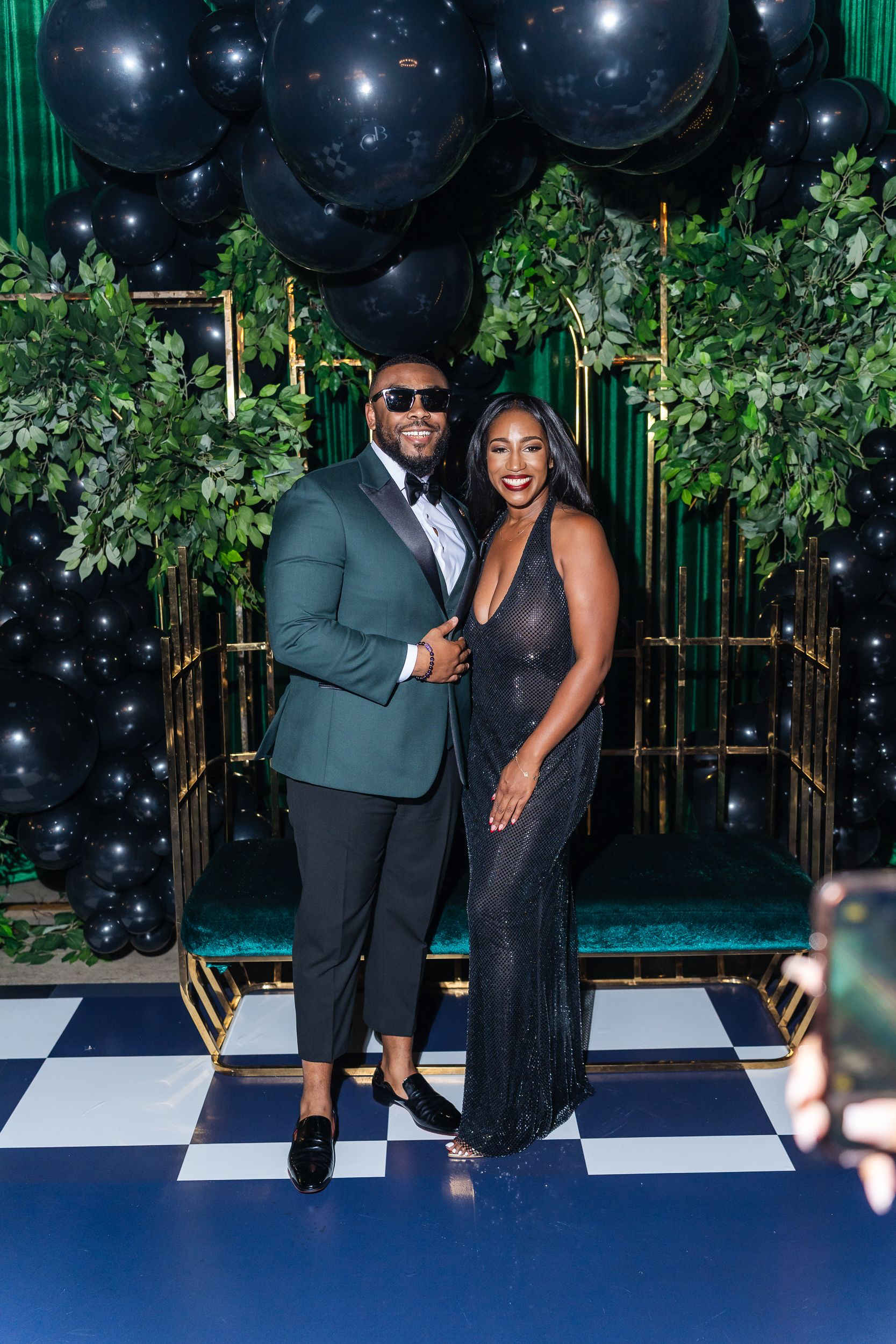 Couple posing in front of a greenery and balloon backdrop at a milestone birthday