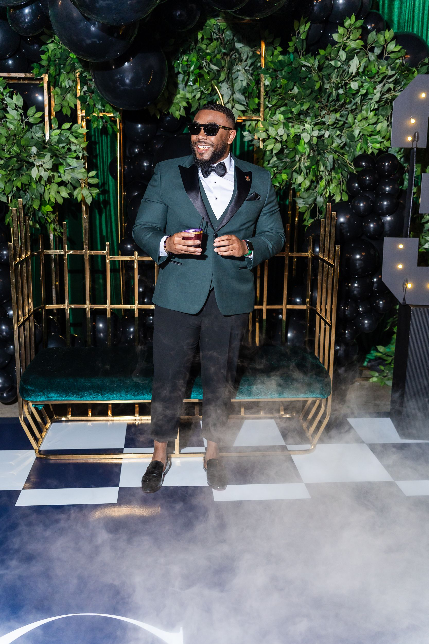 Host in an emerald velvet tuxedo on the black-and-white checkered dance floor