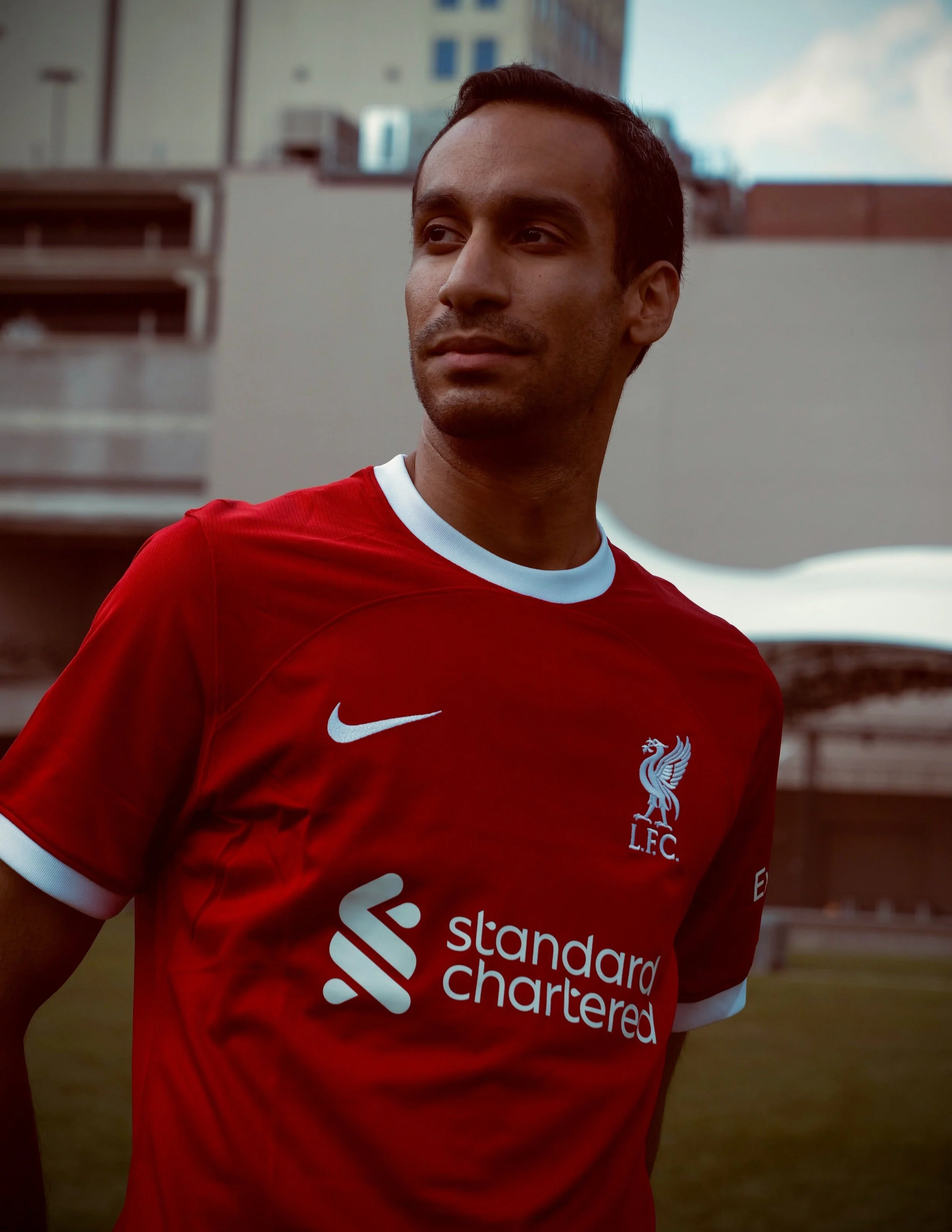 A man wearing a red Liverpool Football Club jersey standing outdoors in an urban area.