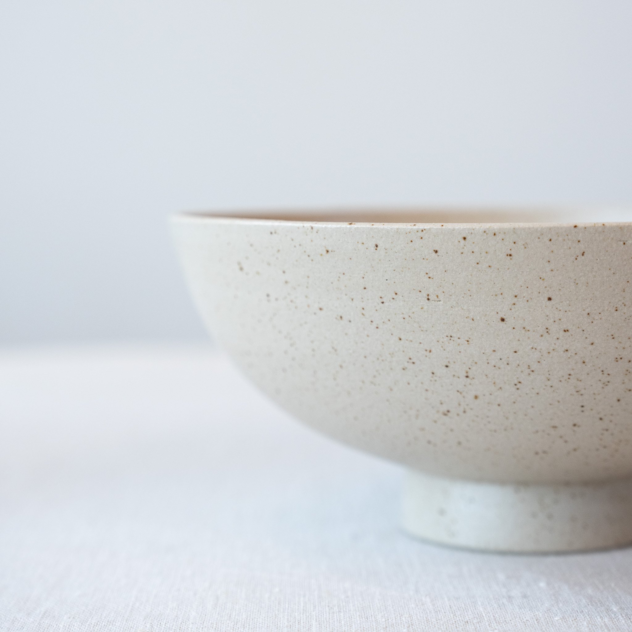 Close-up van een beige keramische kom met spikkelpatroon, minimalistisch ontwerp.