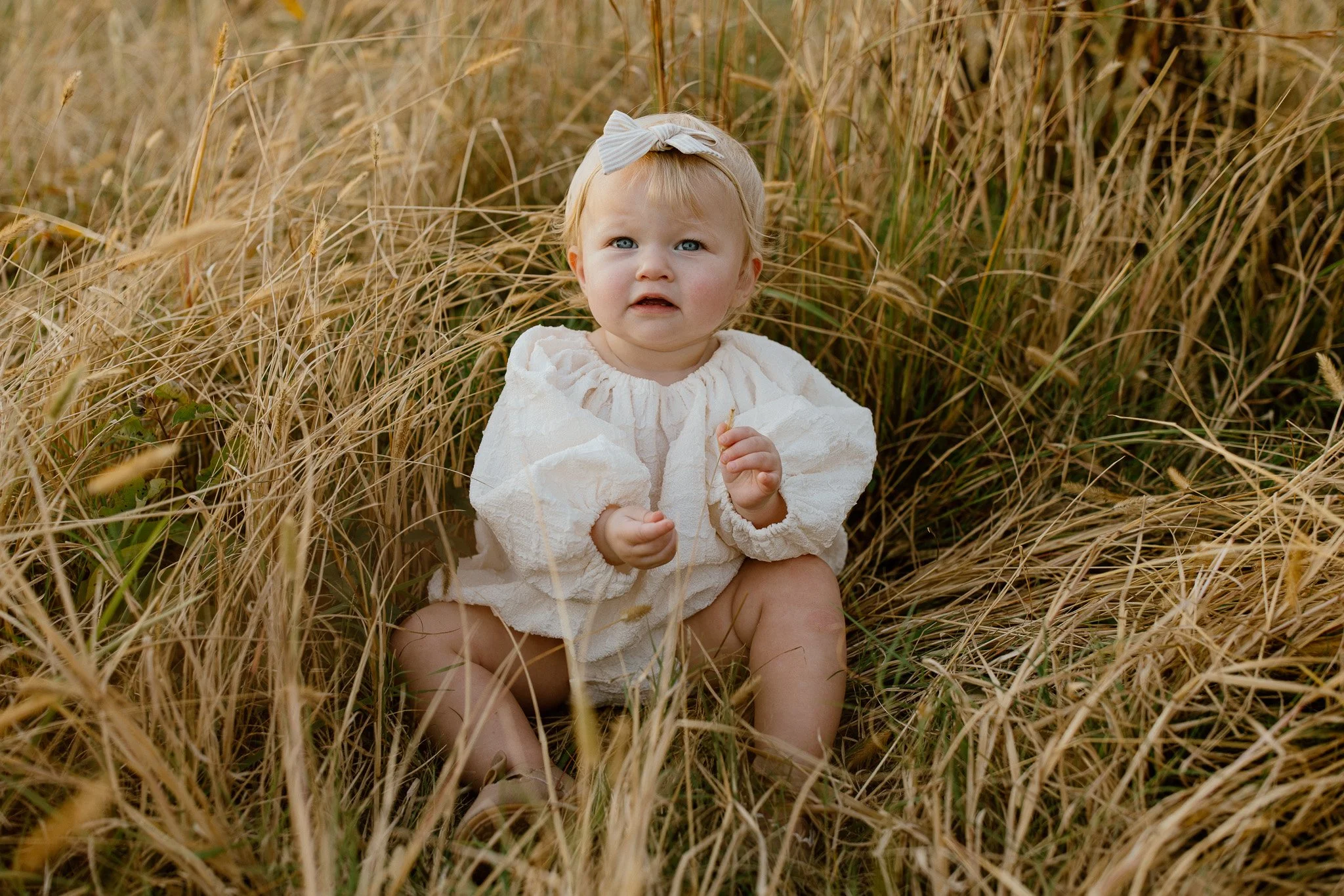 Baby sitting in tall grass during an outdoor family photography session in Tupelo