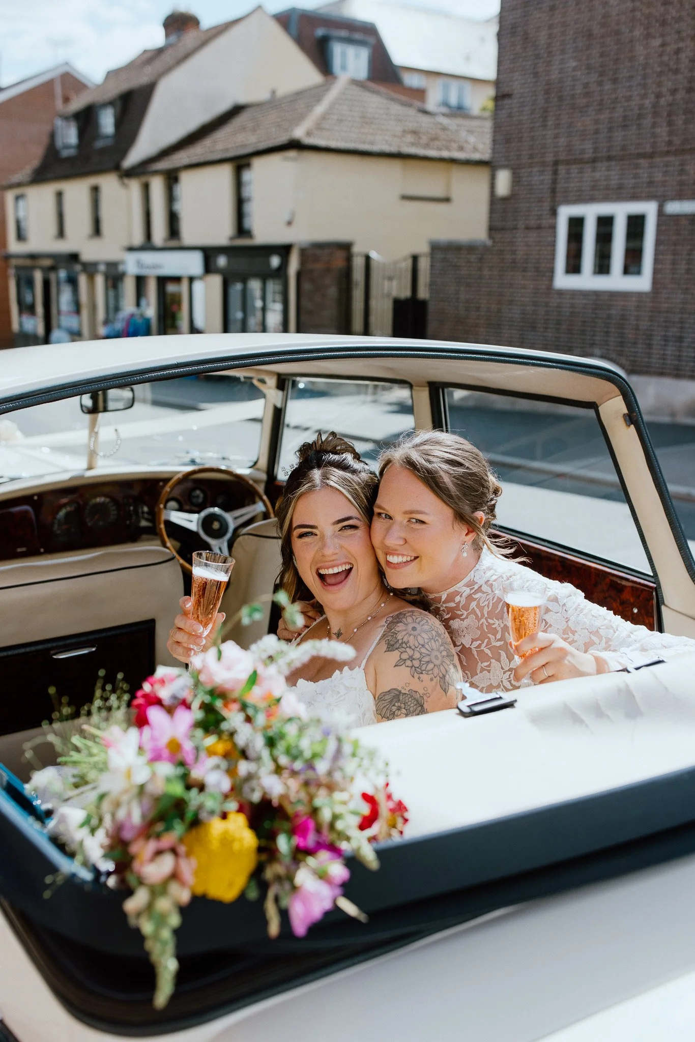 Bride and bride celebrating with champagne in a vintage wedding car in Essex