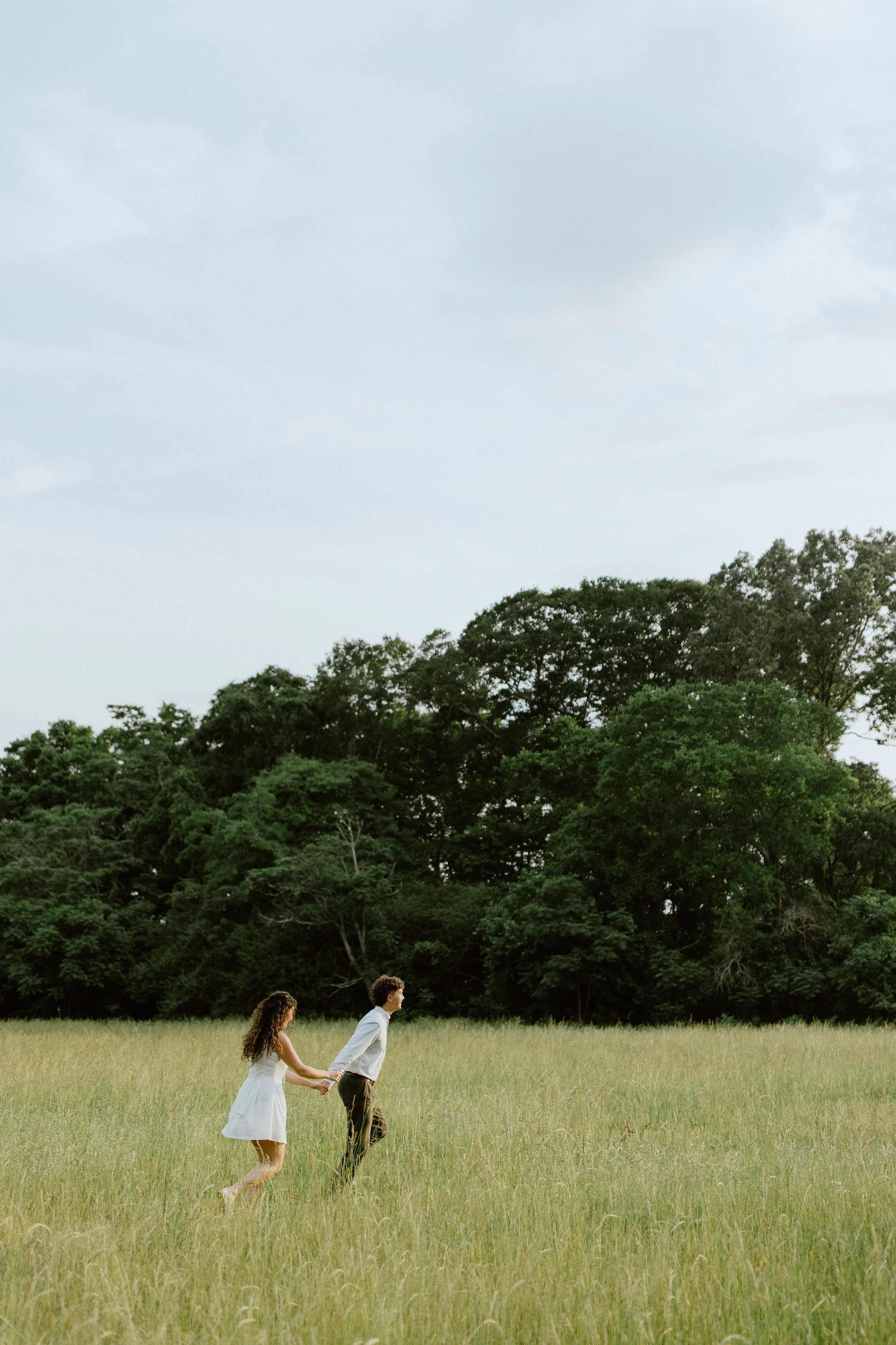 Couple walking hand in hand through a grassy field