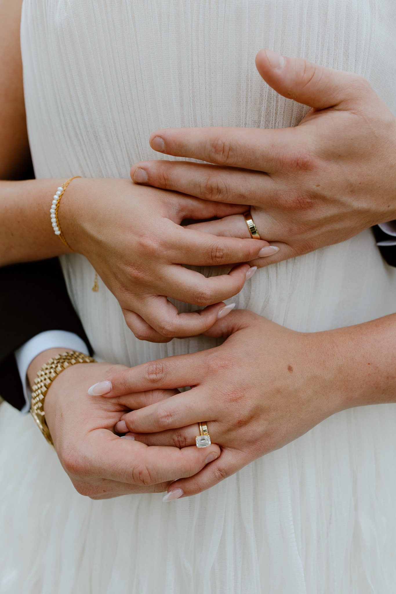 Close-up of hands with rings and jewelry, person wearing white or cream-colored dress with textured fabric.