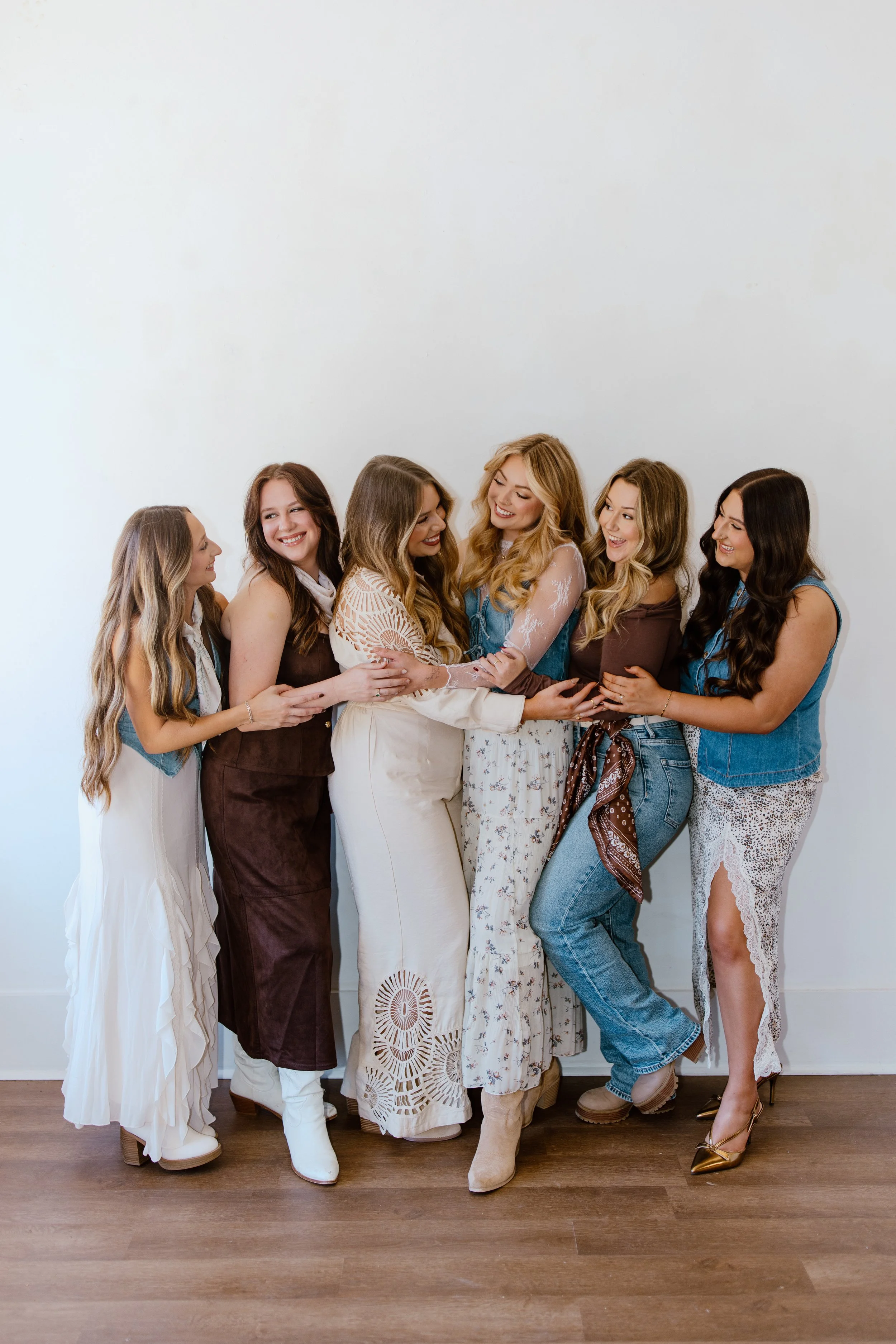 Group of seven women hugging and smiling together against a white wall.