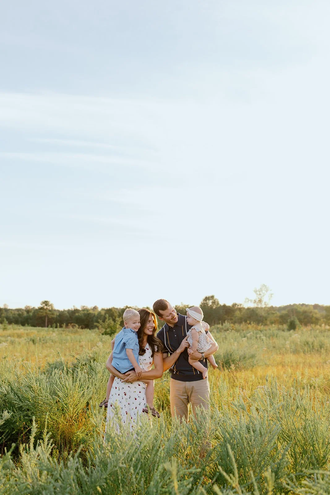 Family of four sharing a candid moment in a field at golden hour