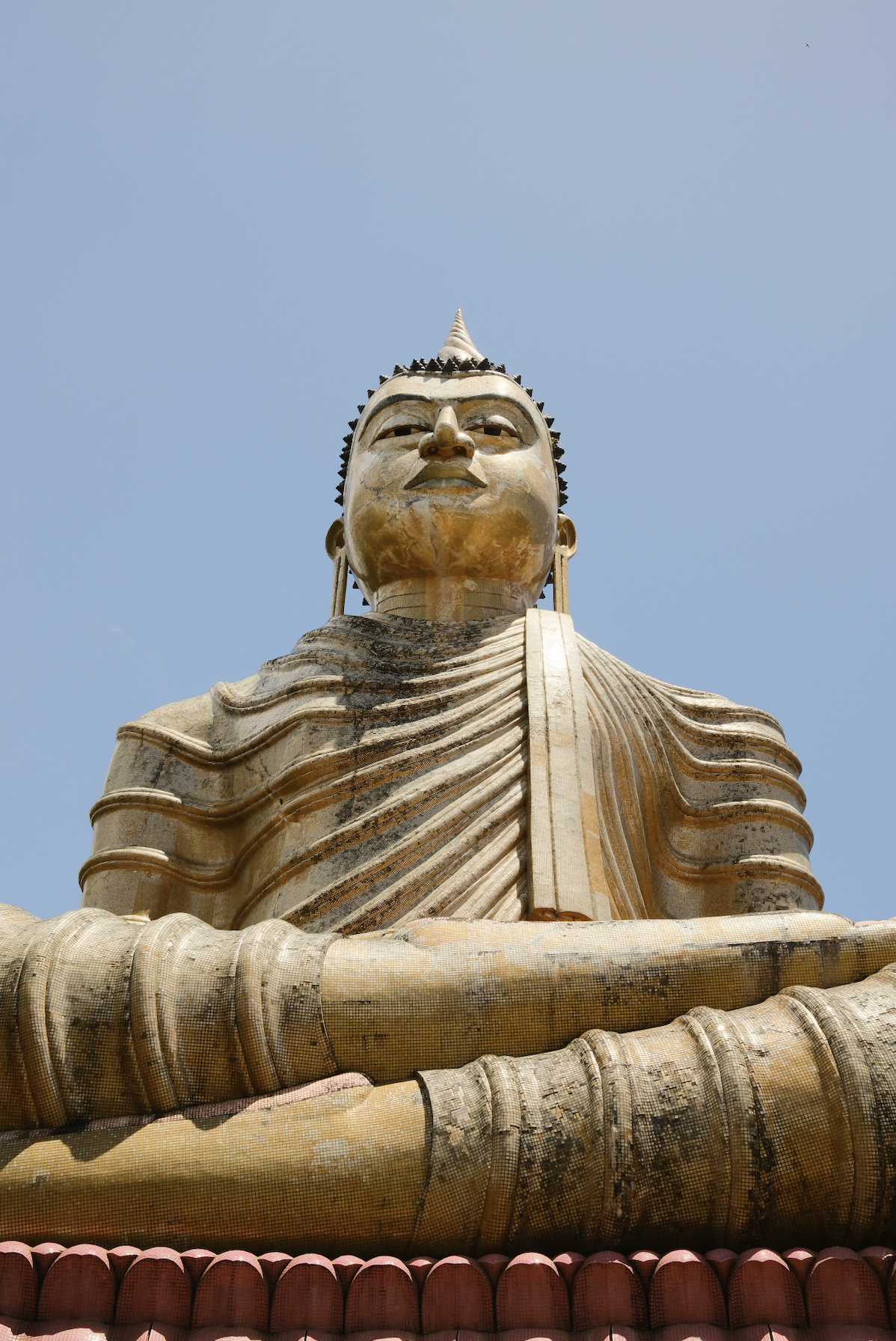 A large golden Buddha statue seated in a meditative pose, with a serene expression, against a clear blue sky.