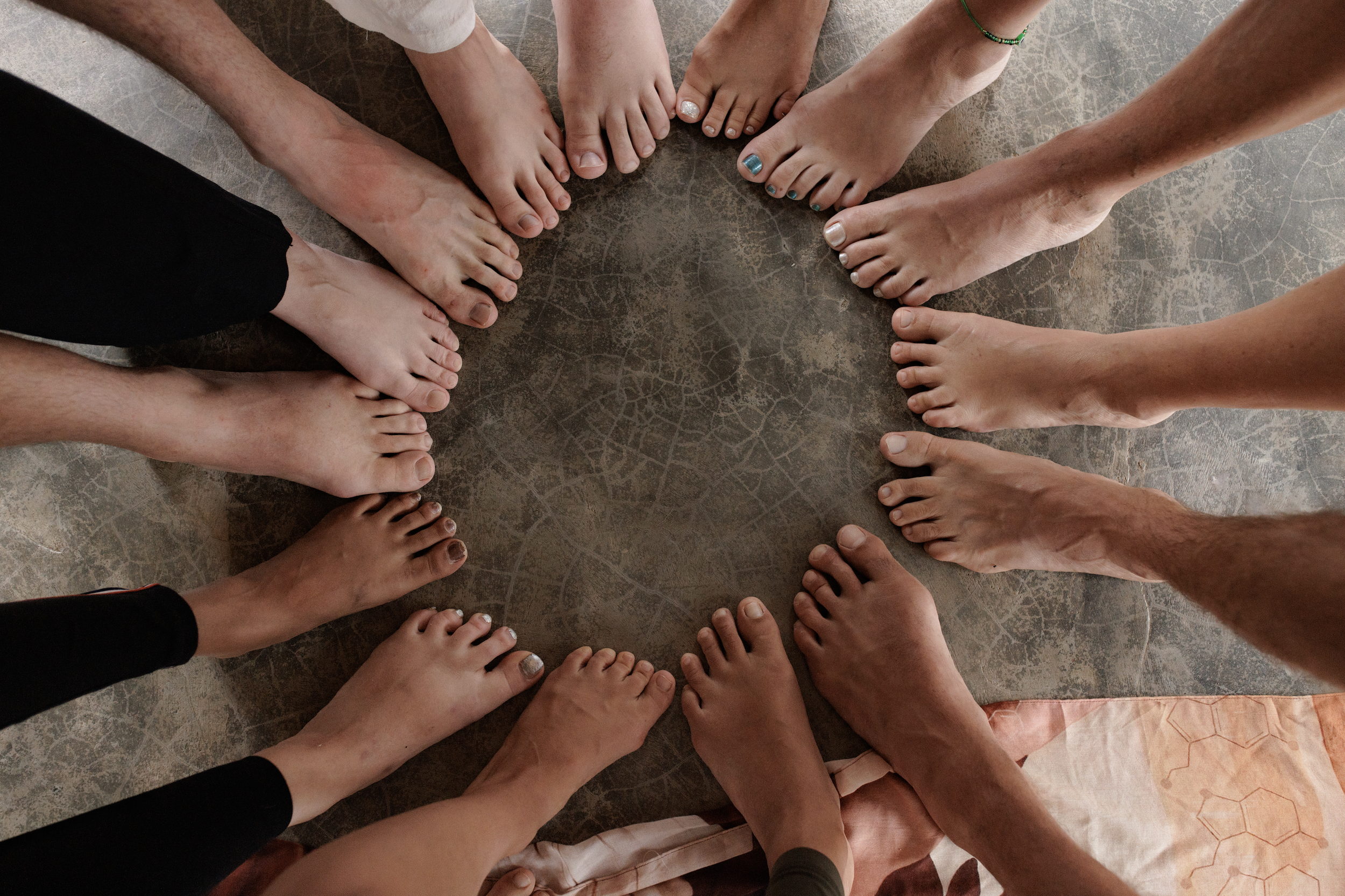 A group of people standing in a circle showing their barefoot feet on a tiled floor.