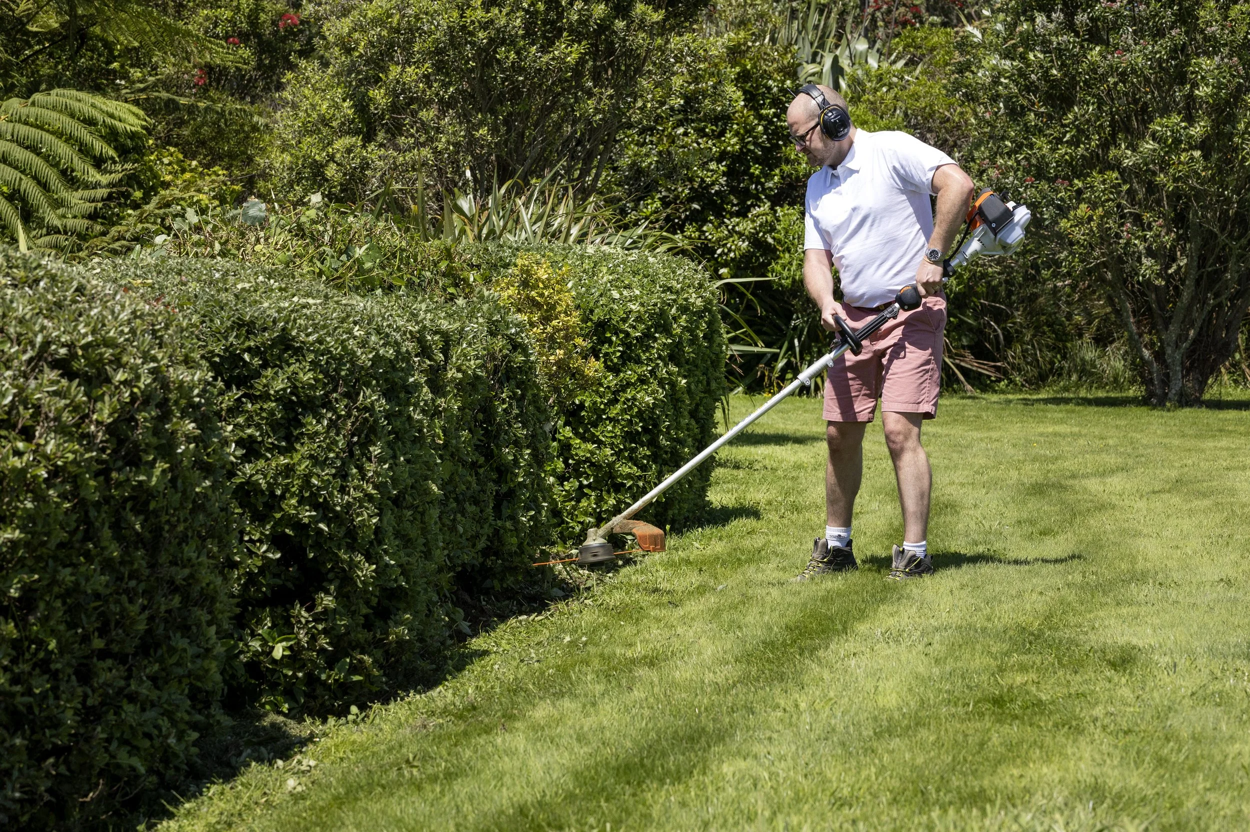 Man trimming bushes with a string trimmer in a garden