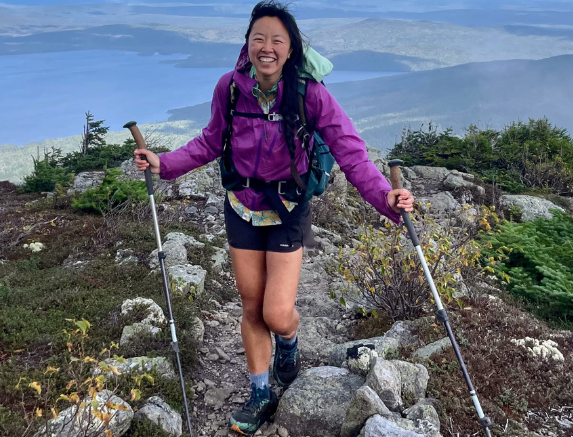 Asian woman hiking on rocky terrain with trekking poles in a mountainous area.