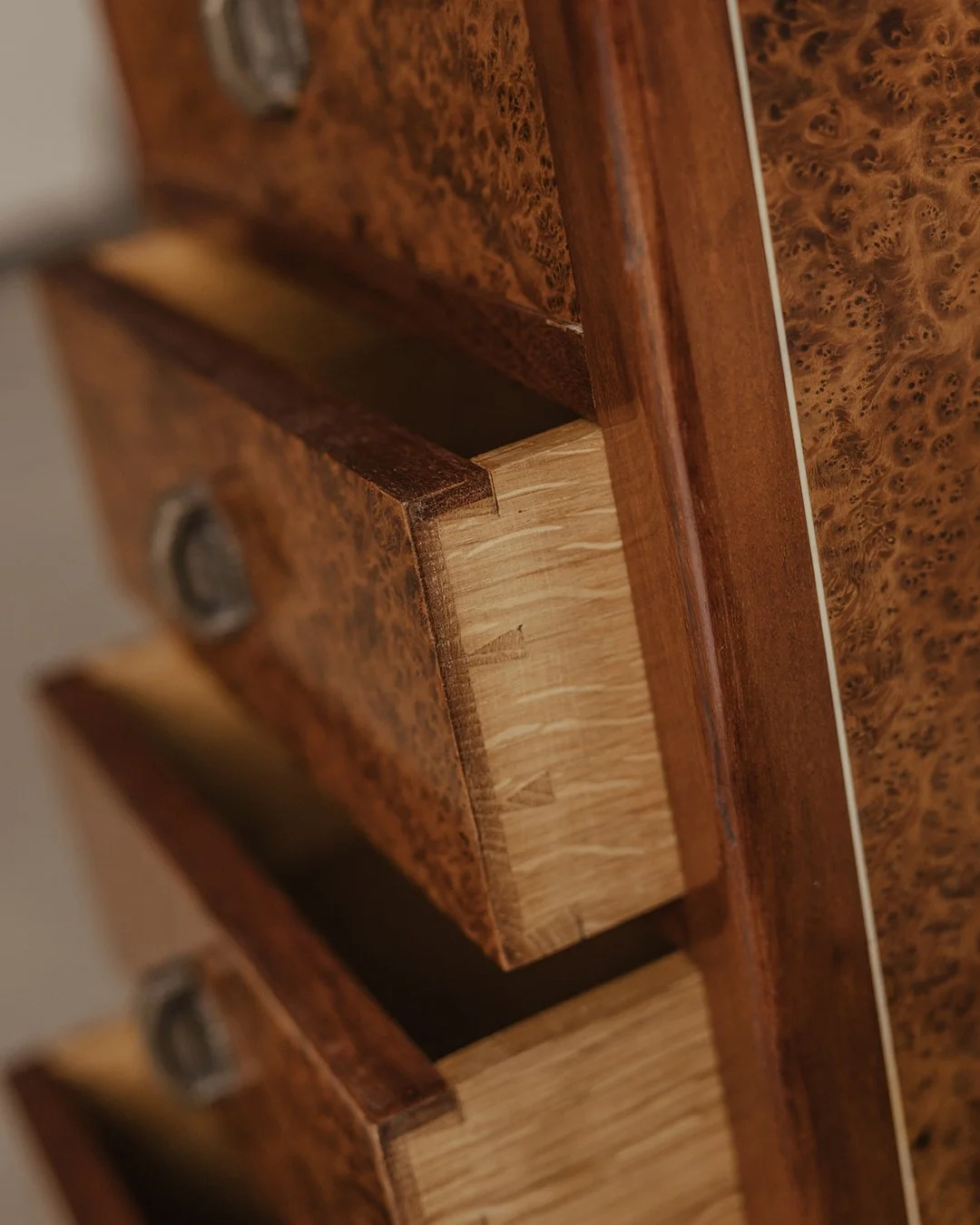 Mid-20th-century Art Deco–inspired burl wood chest of drawers with four stacked drawers, geometric metal handles, and a stepped base