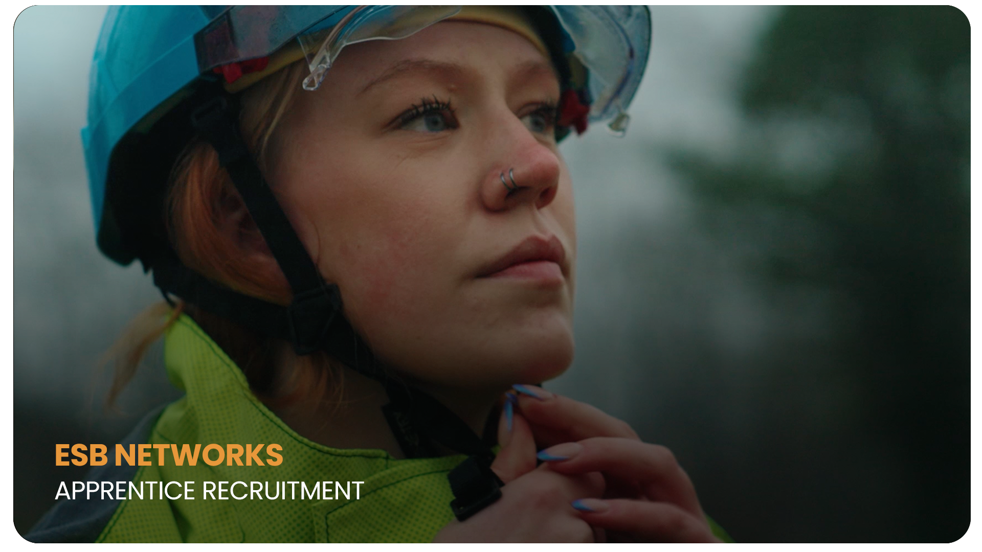 Close-up of a young woman in safety gear, including a helmet and reflective jacket, outdoors, looking thoughtfully into the distance.