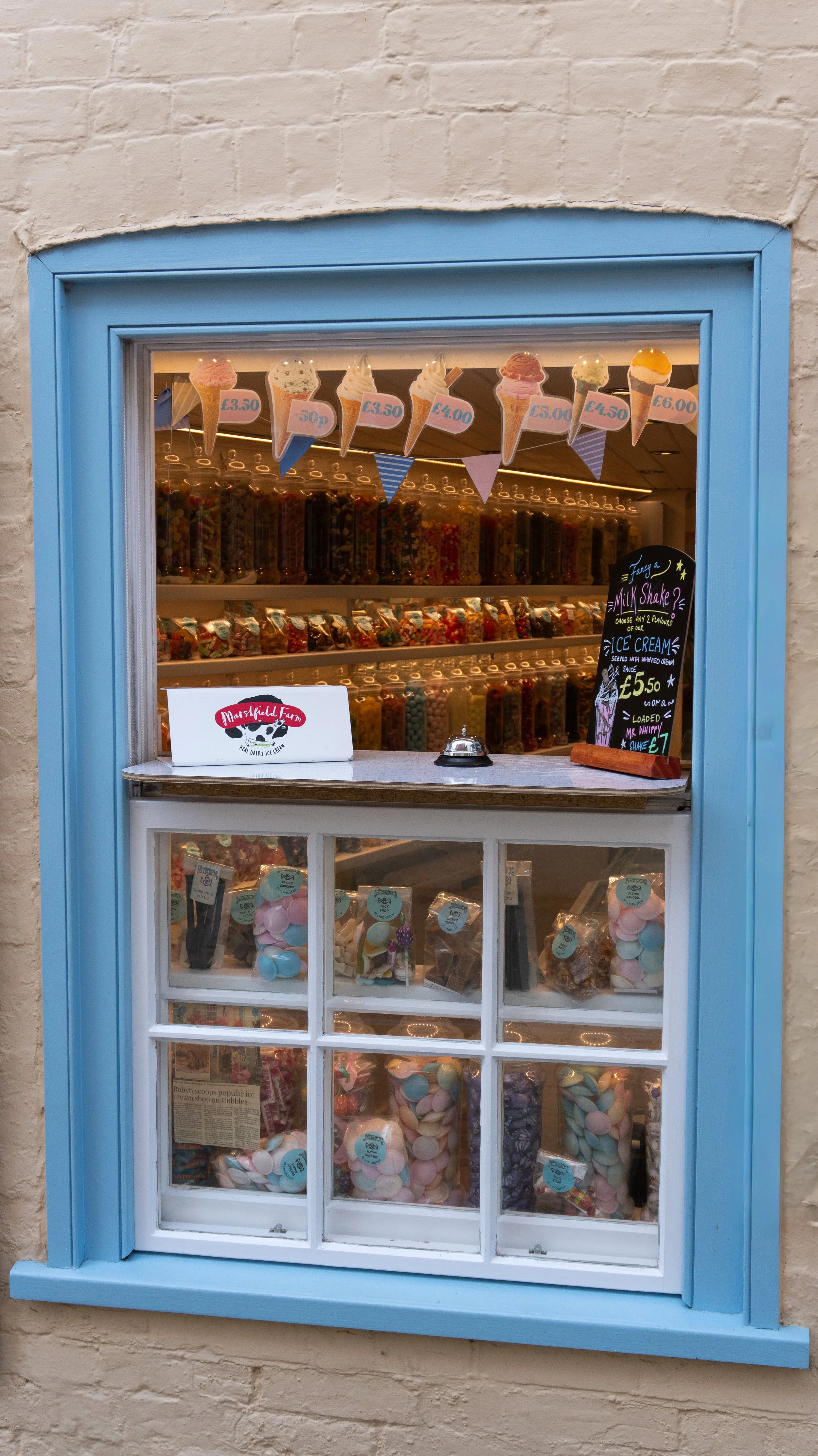 Ice cream shop in Lymington window with various tubs of candies and ice cream cones and signs indicating prices.