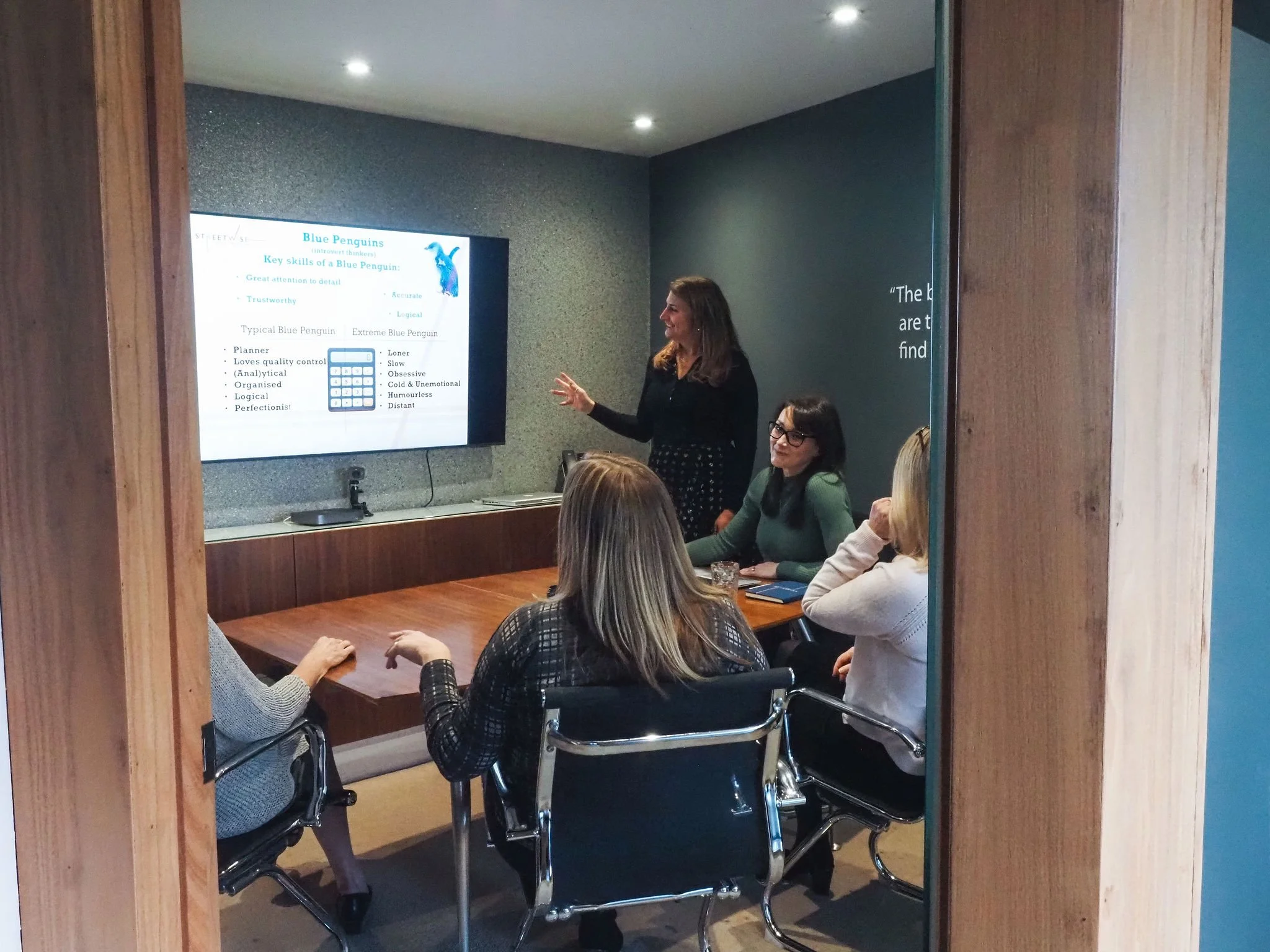 Debbie from Streetwise HR giving presentation in meeting room, viewers seated listening, woman standing near screen displaying slide about Blue Penguins.