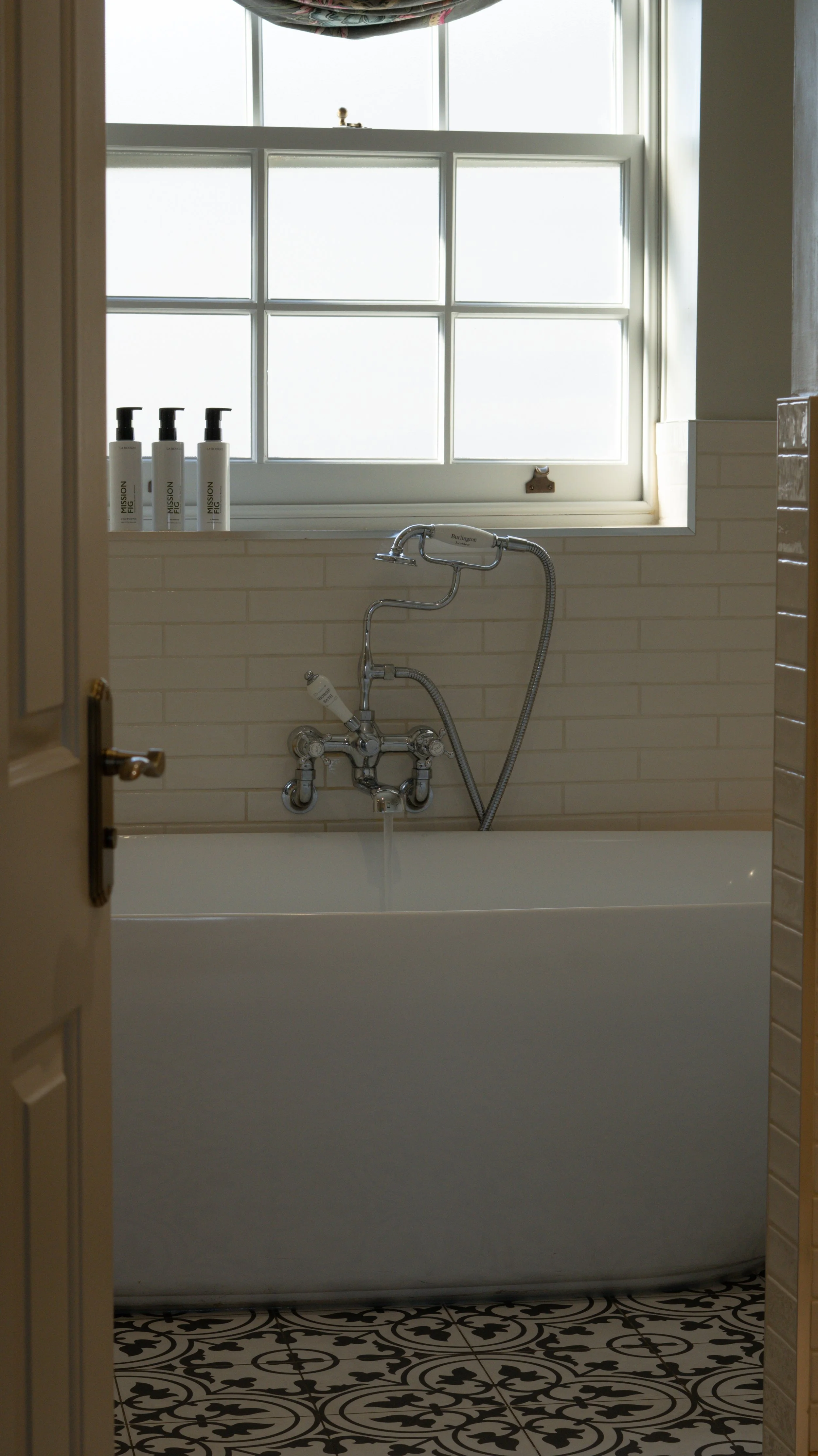 Bathroom at Stanwell House with a window, bathtub, and vintage-style patterned floor tiles.