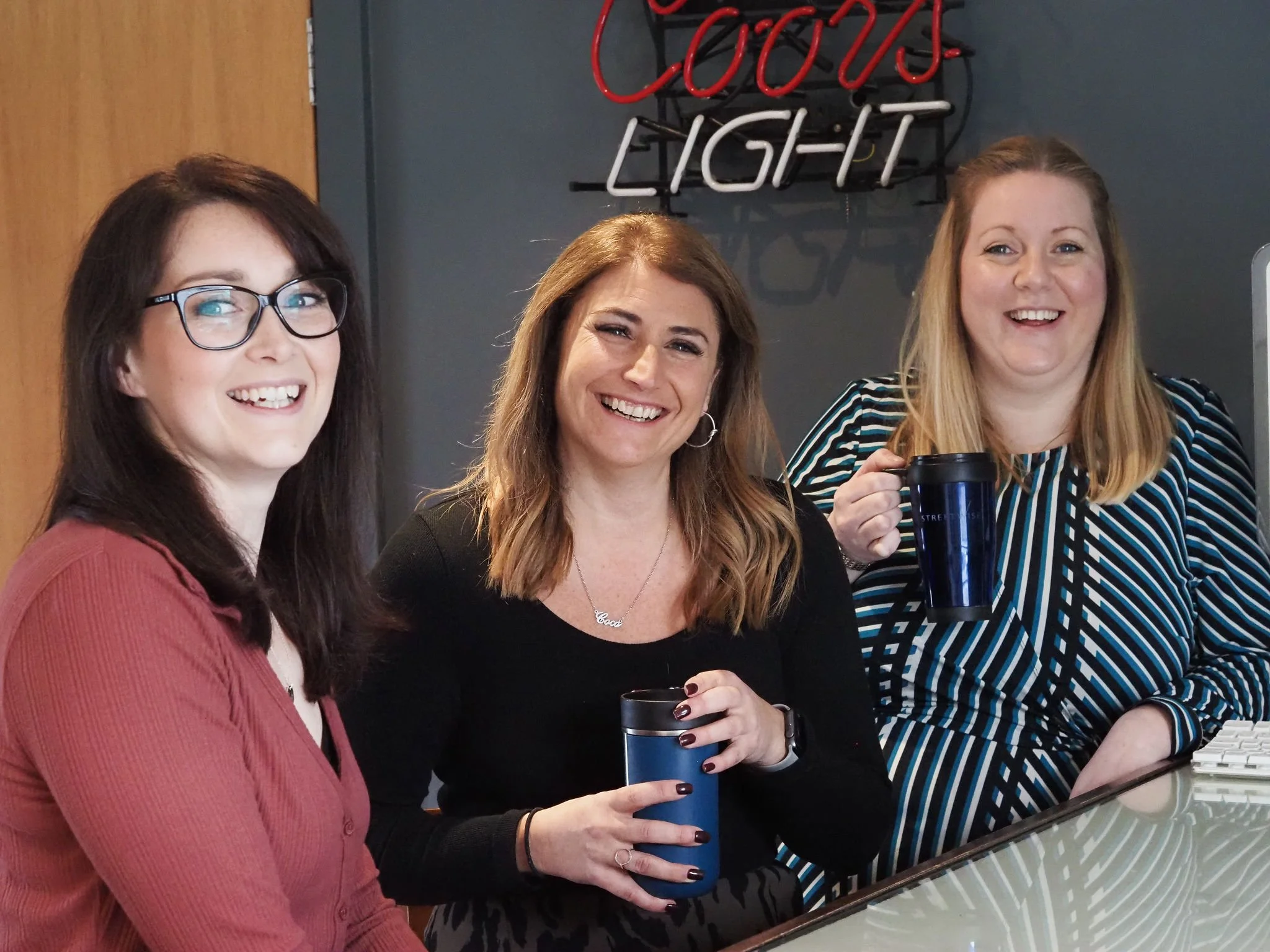 Streetwise HR Gurus smiling and holding coffee cups in an office.