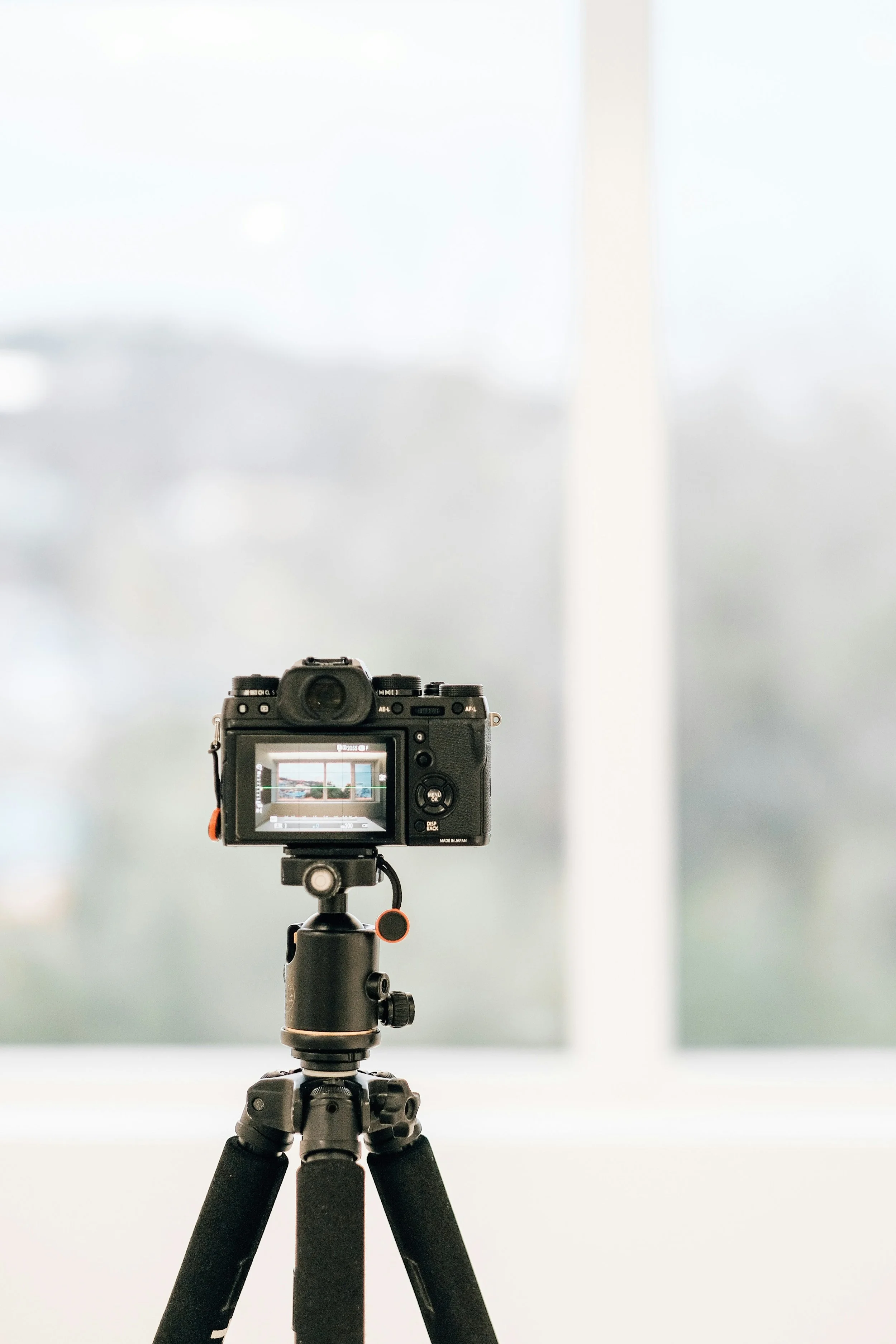 A professional digital camera mounted on a tripod, facing towards a plain white background.