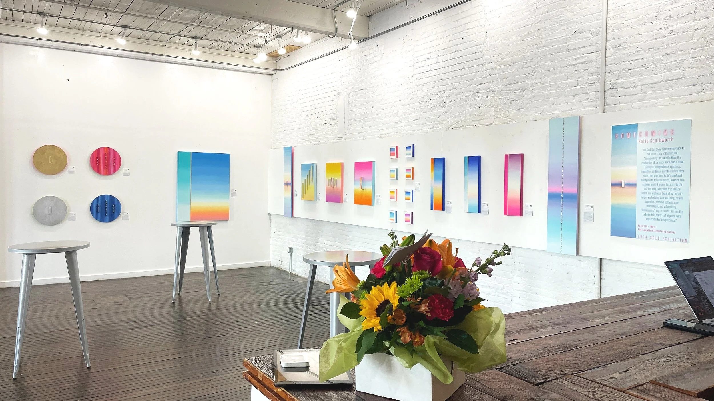 Armstrong Gallery at The Knowlton featuring abstract artwork installation, white walls, wood table with florals, and gallery seating