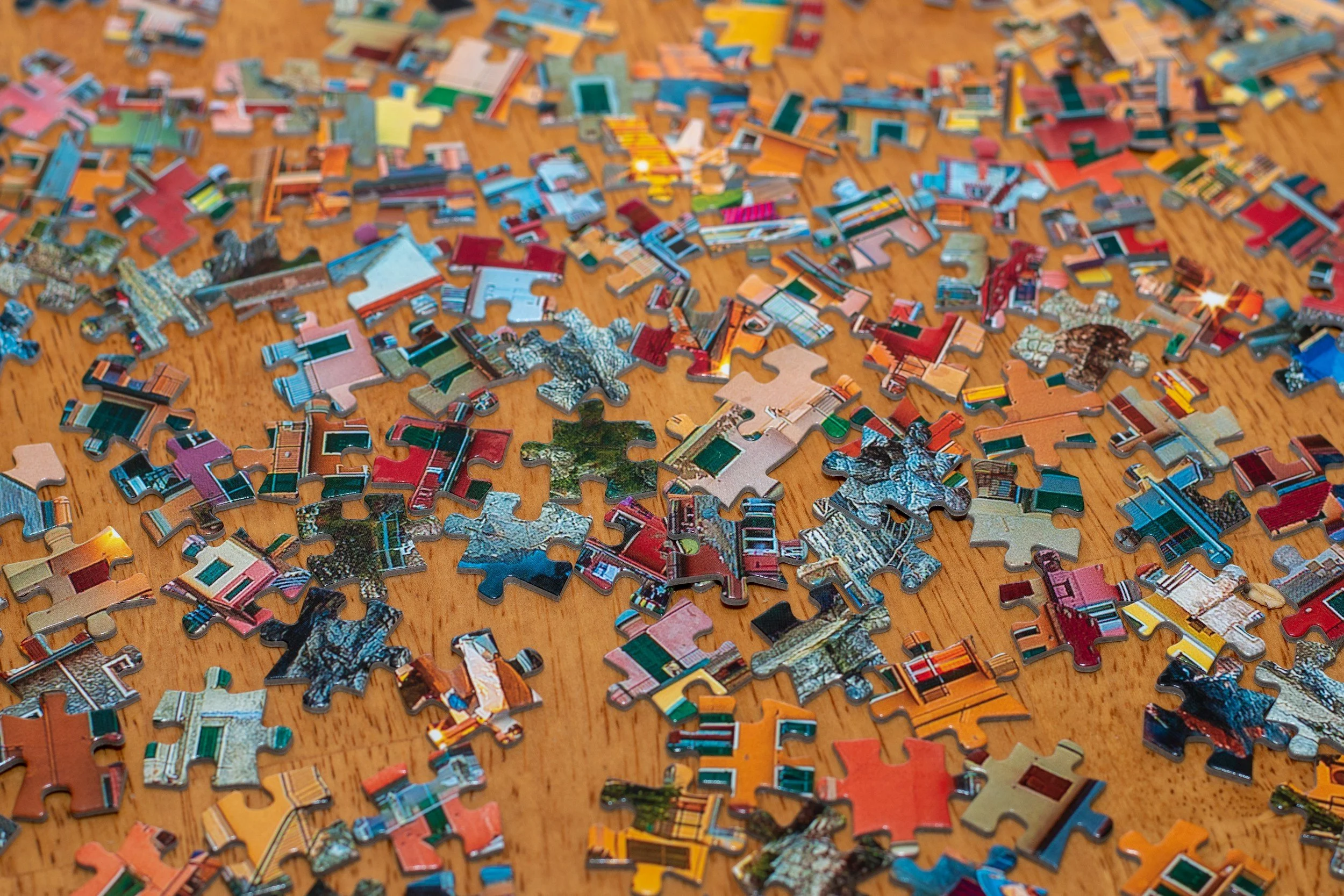 A wooden tabletop is covered with brightly colored puzzle pieces.