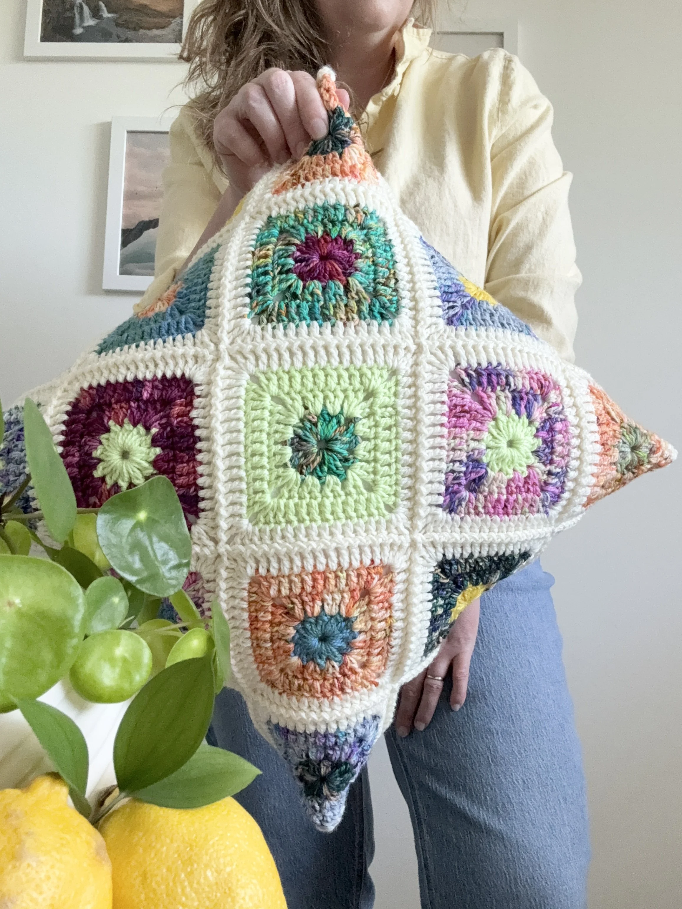 Mallory holding a brightly colour pillow with star centered granny squares featuring the Limoncello mini set collection by Hue Loco Yarn