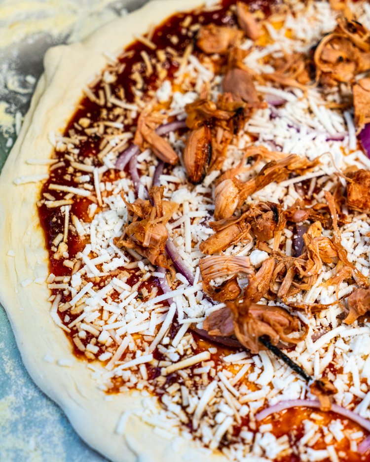  The beginning stages of our Vegan BBQ Jackfruit pizza, featuring vegan cheese and marinated shredded jackfruit pieces. 