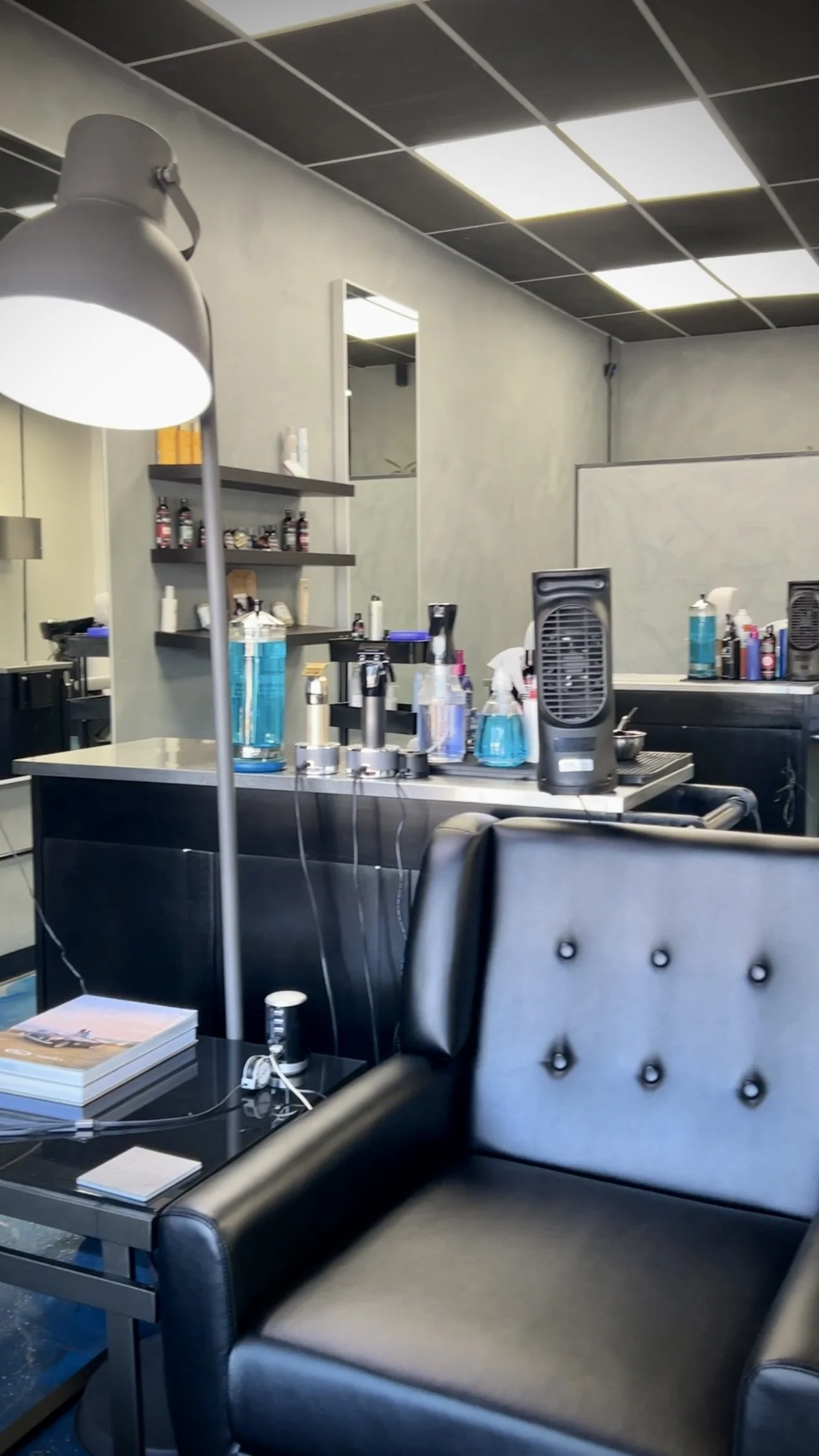 Salon with black leather chairs, styling tools, bottles of water, and hair products on shelves.